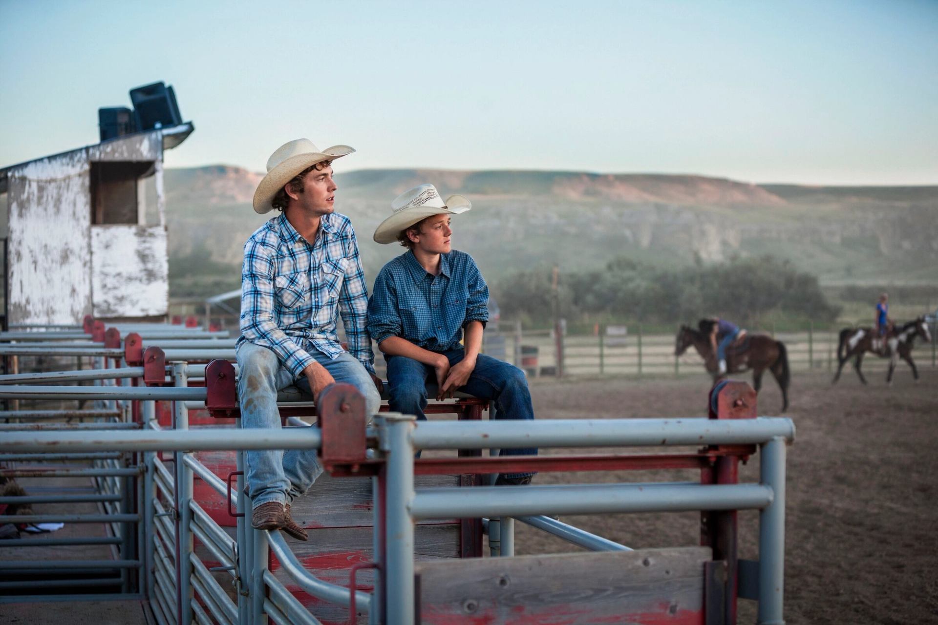 Cowboys sitting on gate at rodeo