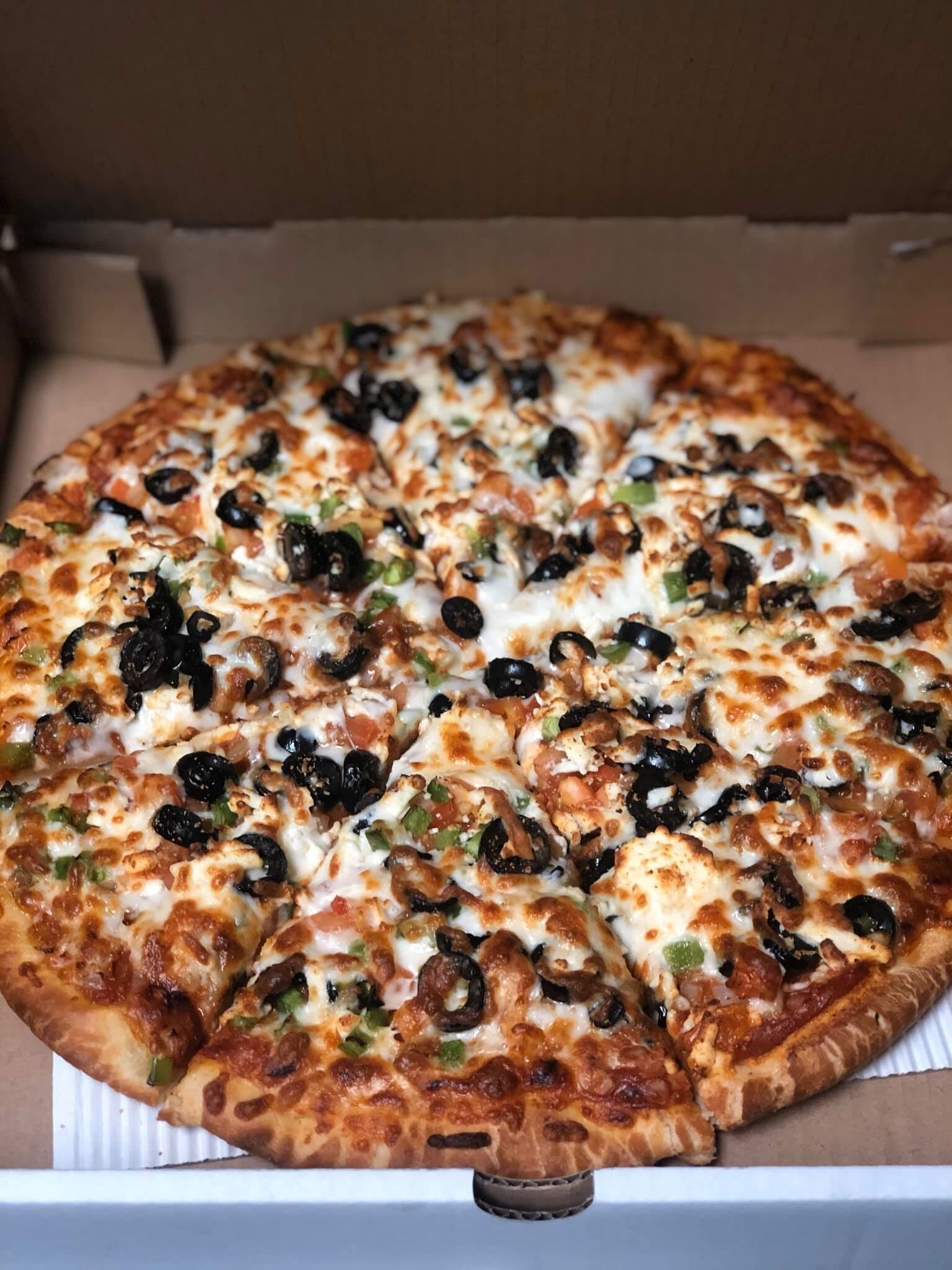 Fresh pizza with cheese, olives, and peppers in a box at Piccolos Pizza & Pasta.