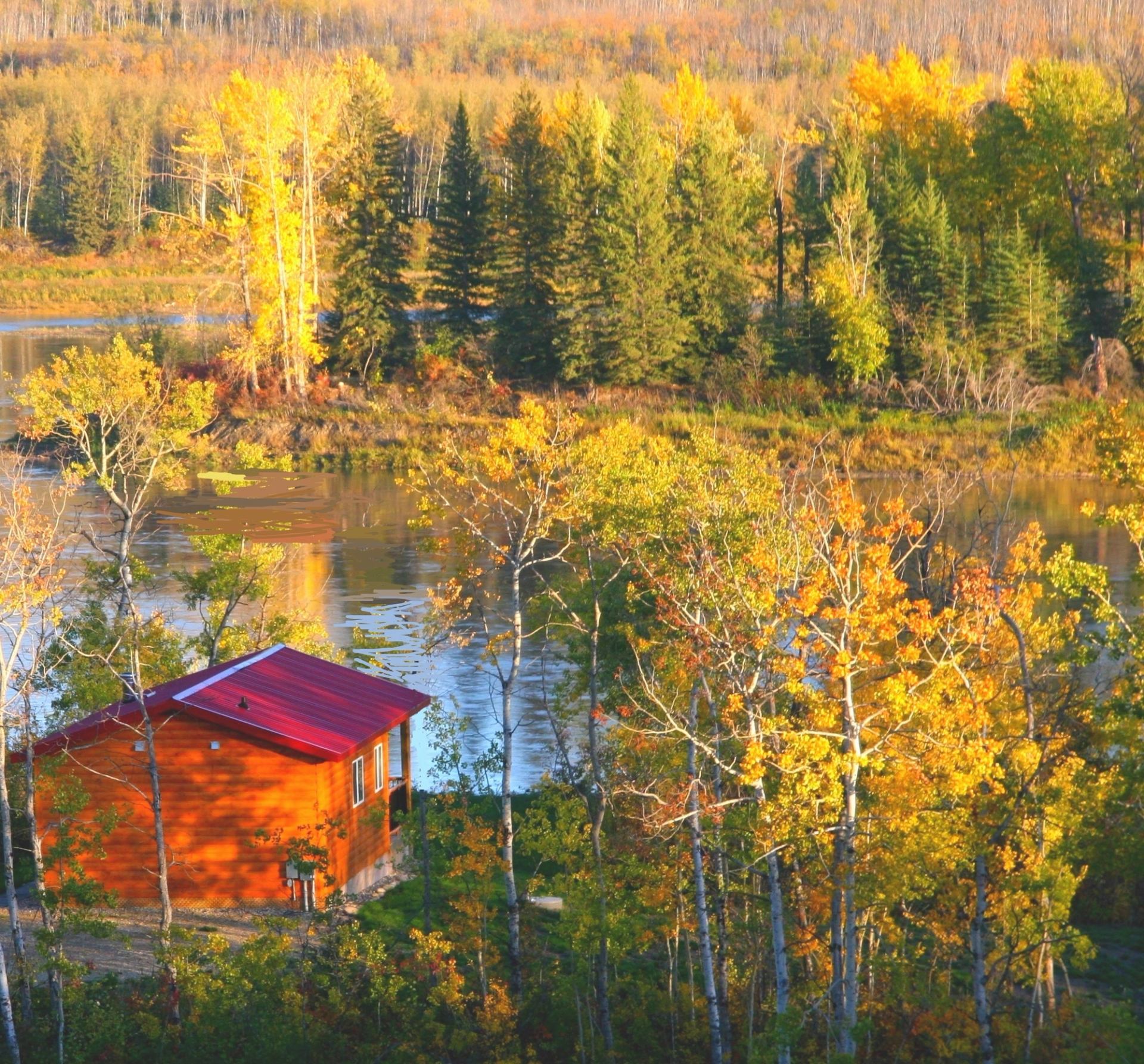 Small wooden cabin with red roof surrounded by colorful fall trees near a river