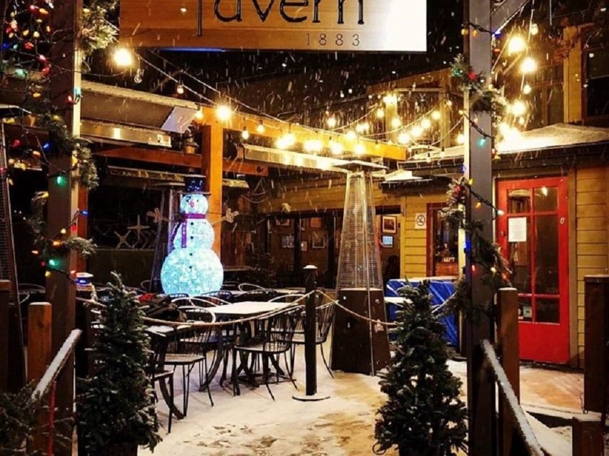 Snowy patio at Tavern 1883 lit with string lights and festive decorations on a winter night.