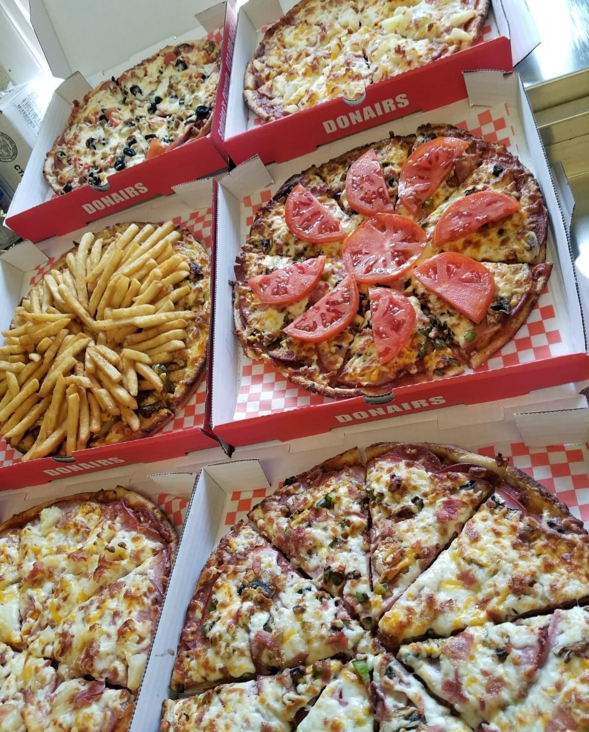 Six pizza boxes with assorted toppings and a box of fries arranged for sharing.