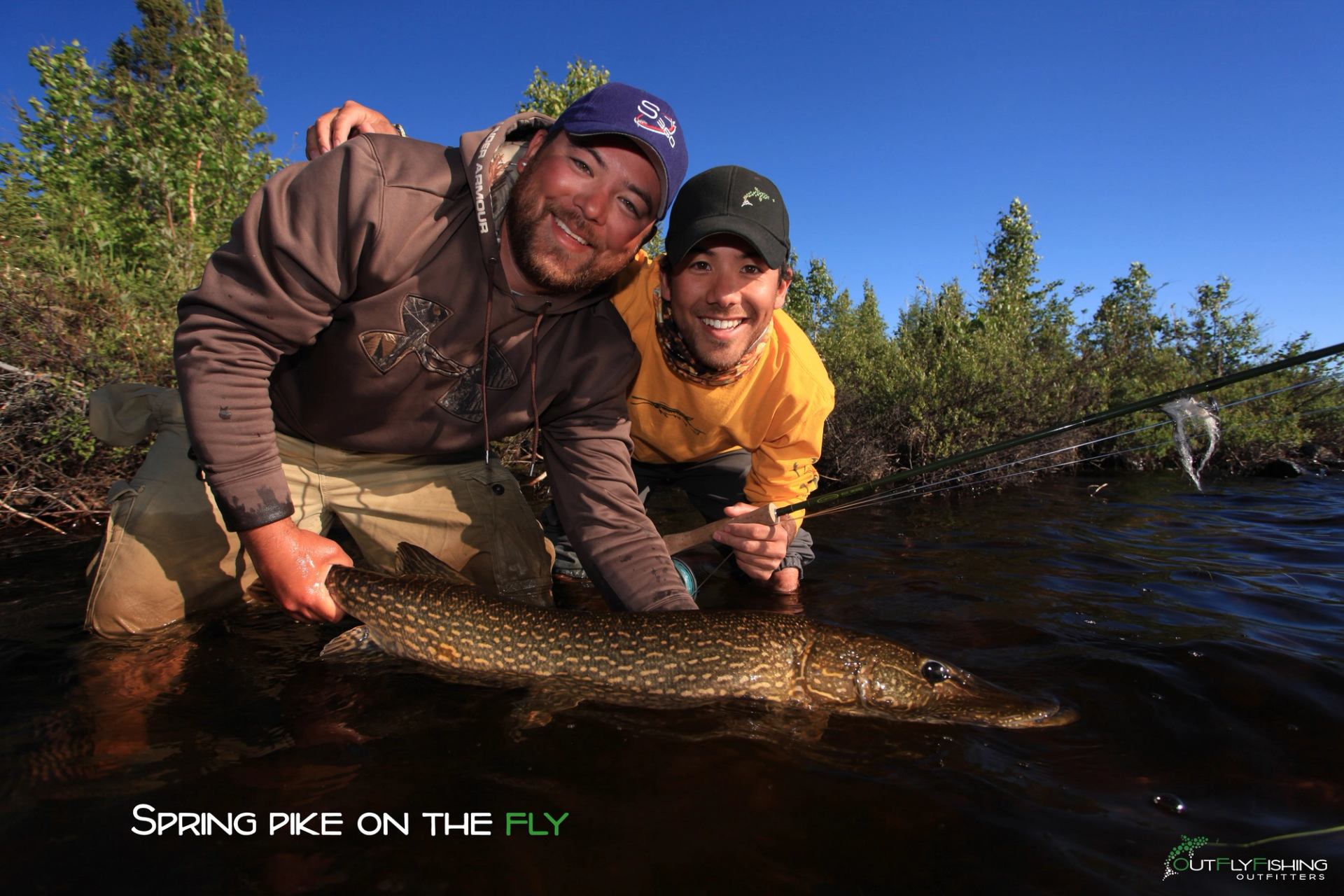 Two anglers smile while releasing a northern pike during a spring fly fishing trip.