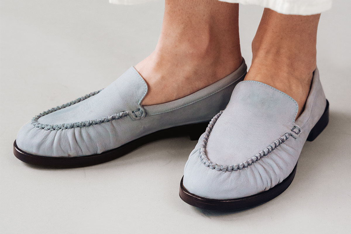 Light blue loafers with stitched toe detail, worn with light-colored outfit.