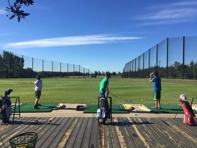 Three golfers practicing swings at Raven Crest driving range."