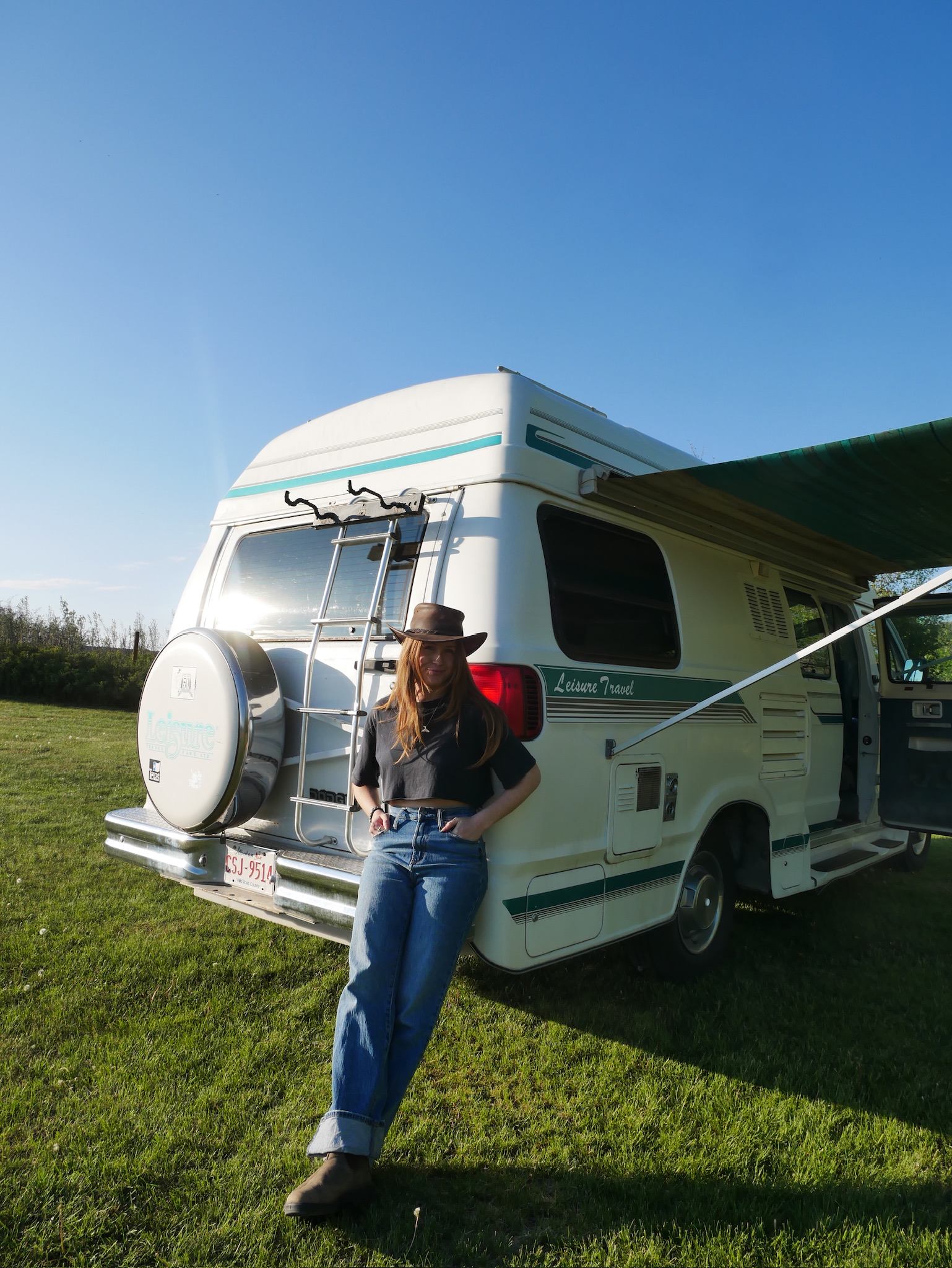 White camper van with awning on grassy field under clear blue sky.