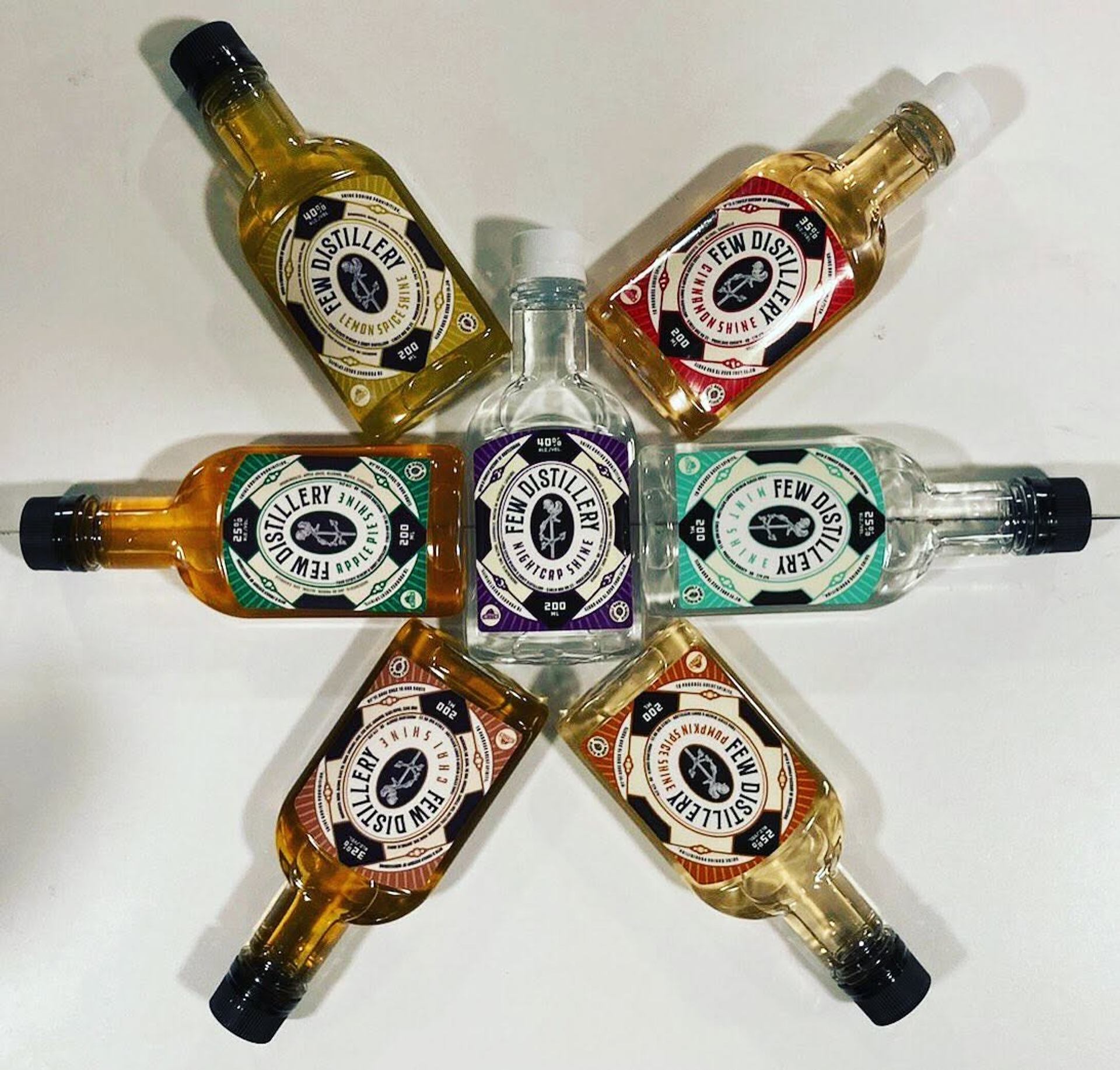 Bottles of handcrafted spirits form a star-shaped arrangement on a white background for display.