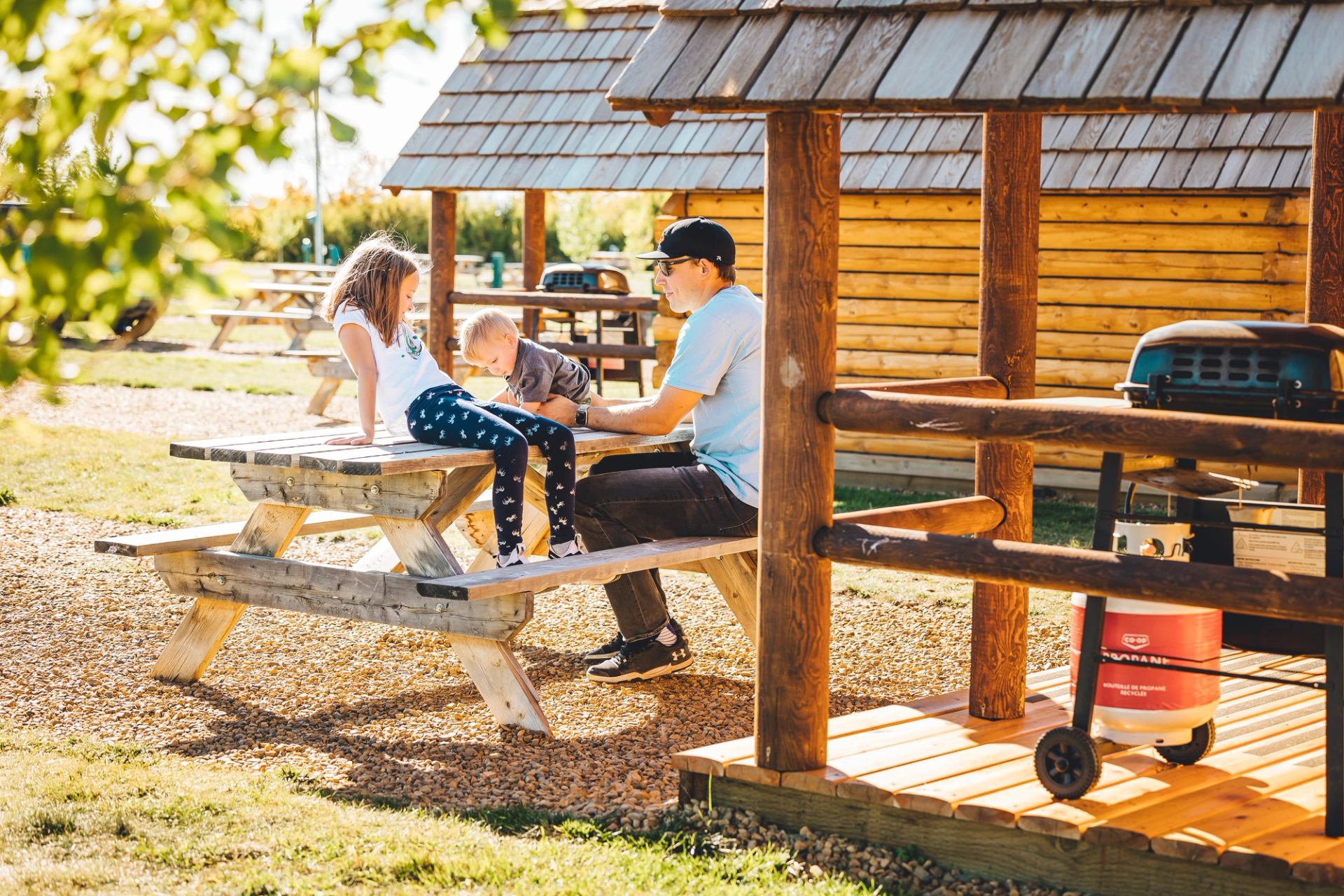 Campground with picnic tables, shelters, grill, and people enjoying the outdoors.