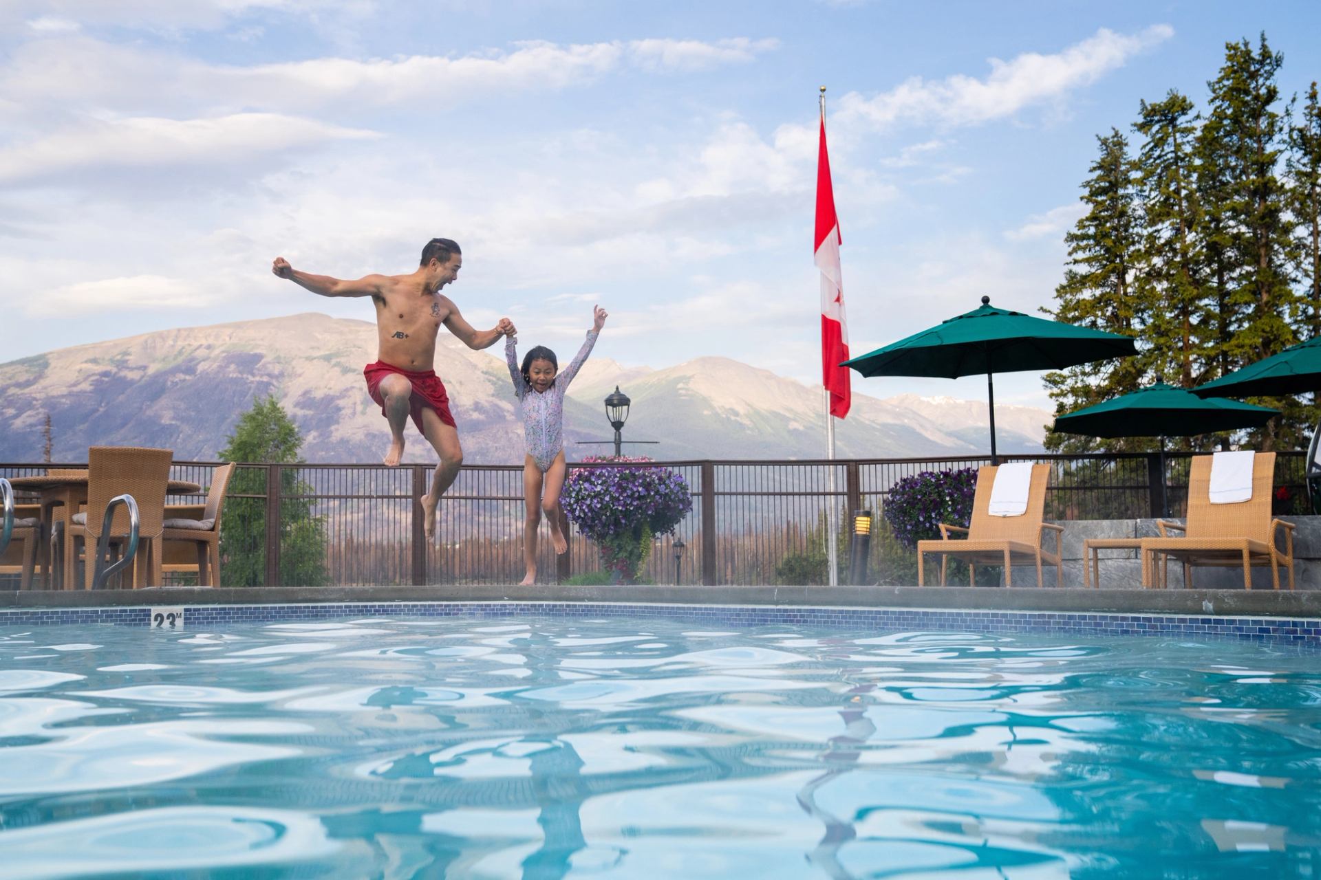 Father and daughter jumping into the all-seasons outdoor heated pool at Fairmont Jasper Park Lodge.