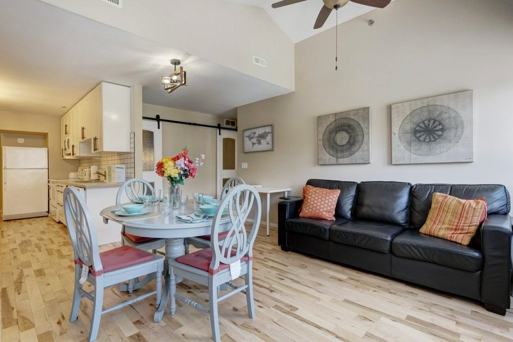 Open living space with black leather sofa, round dining table, and bright kitchen.