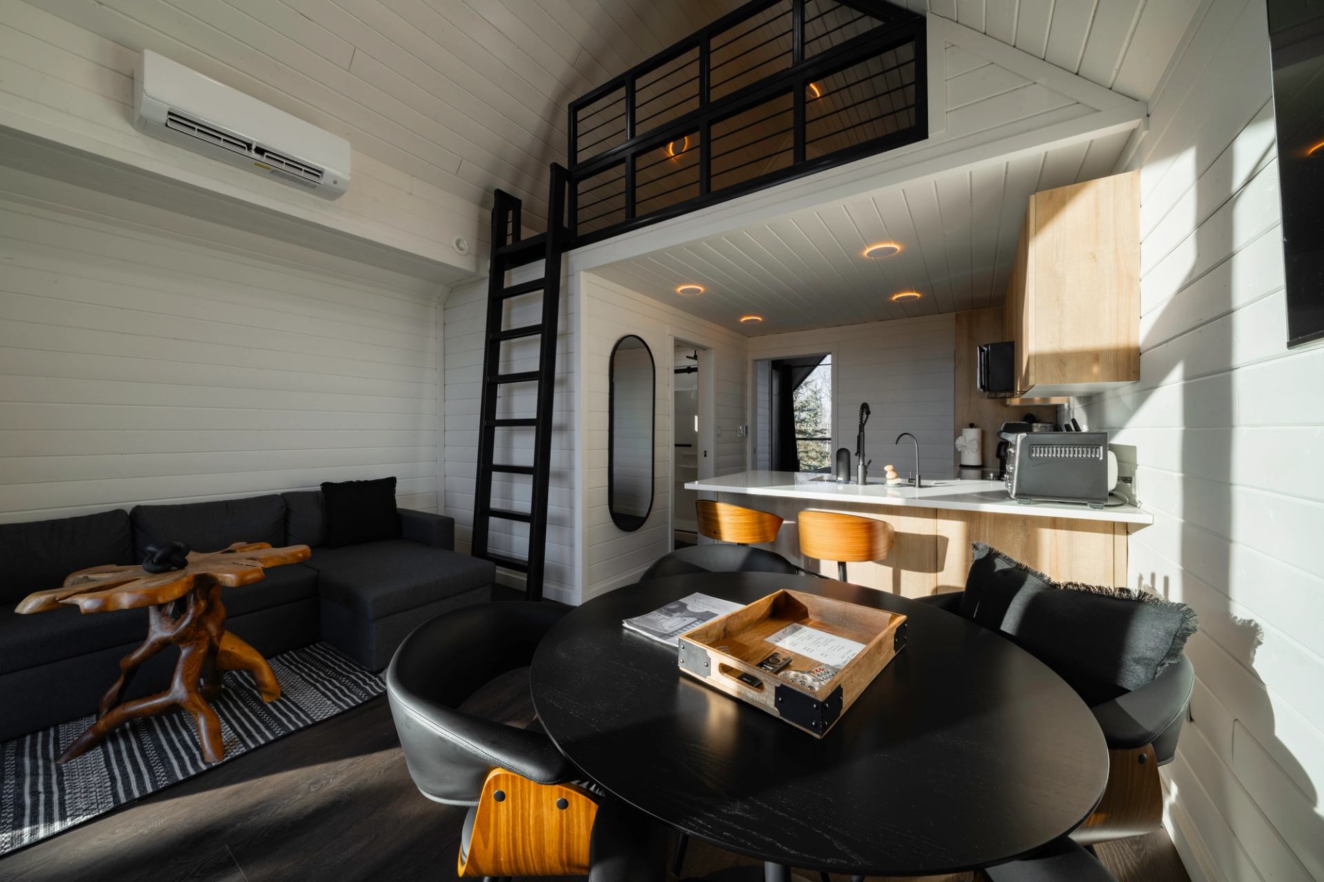 Modern tiny home interior with loft, kitchen island, dining table and grey sectional sofa.