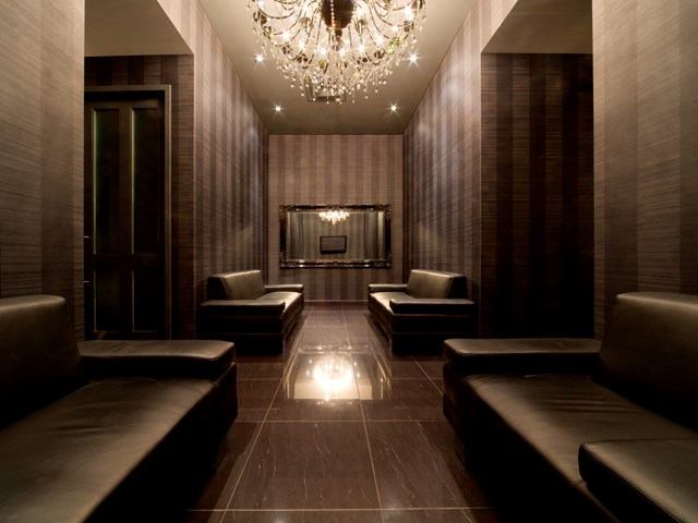 Luxurious salon lounge with leather seating, glossy floors, soft lighting, and a crystal chandelier.