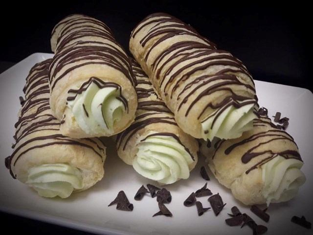 Cream-filled pastry rolls with chocolate drizzle on white plate with chocolate shavings.
