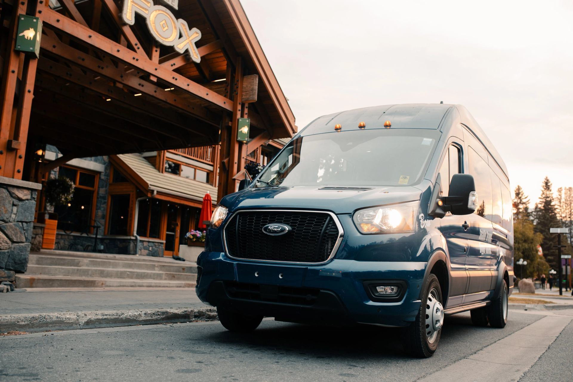 Blue Ford passenger van parked outside Fox lodge-style building with wooden beams.