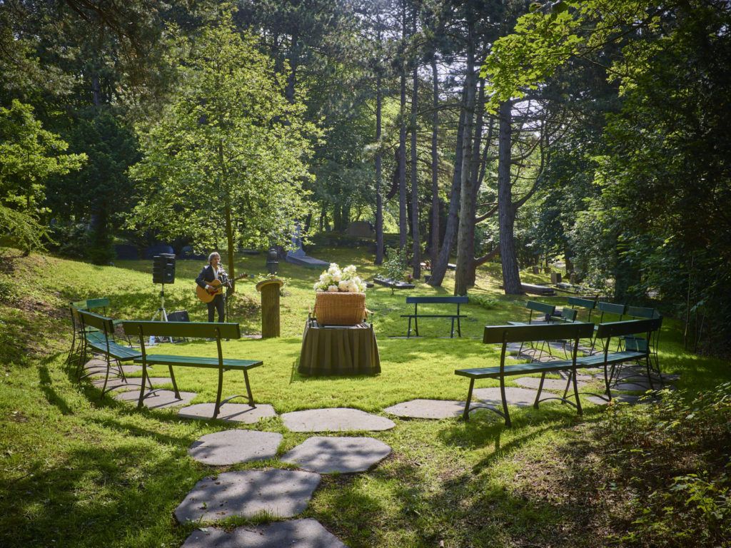 Bankjes in een kring om een rieten kist met witte bloemen, op een open plek in het bos