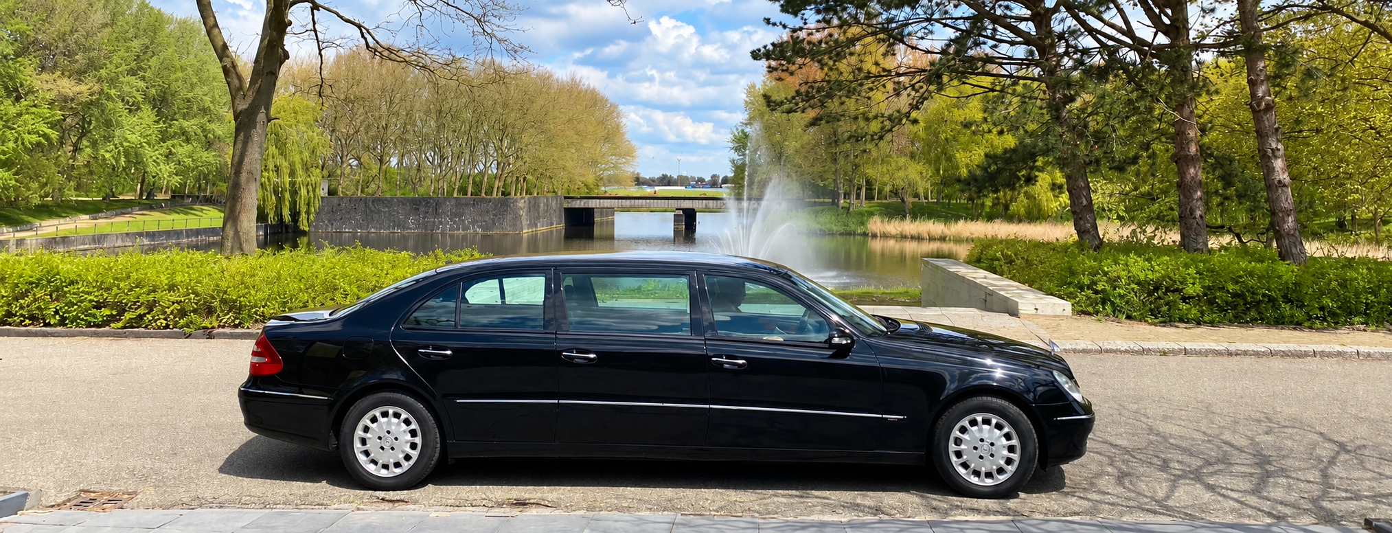 Een zwarte volgauto op een pad bij Westgaarde, met een vijver en een fontein erachter