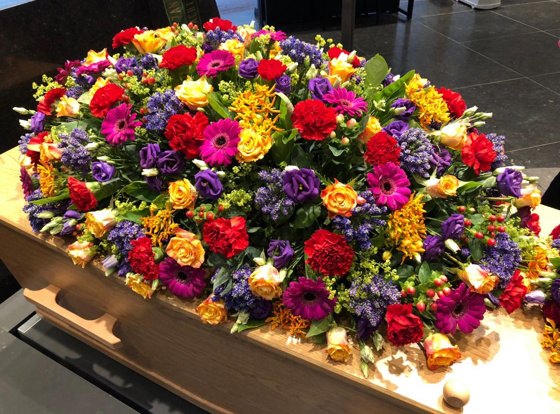 Een uitvaartkist met een groot bloemstuk in rood, geel en paars