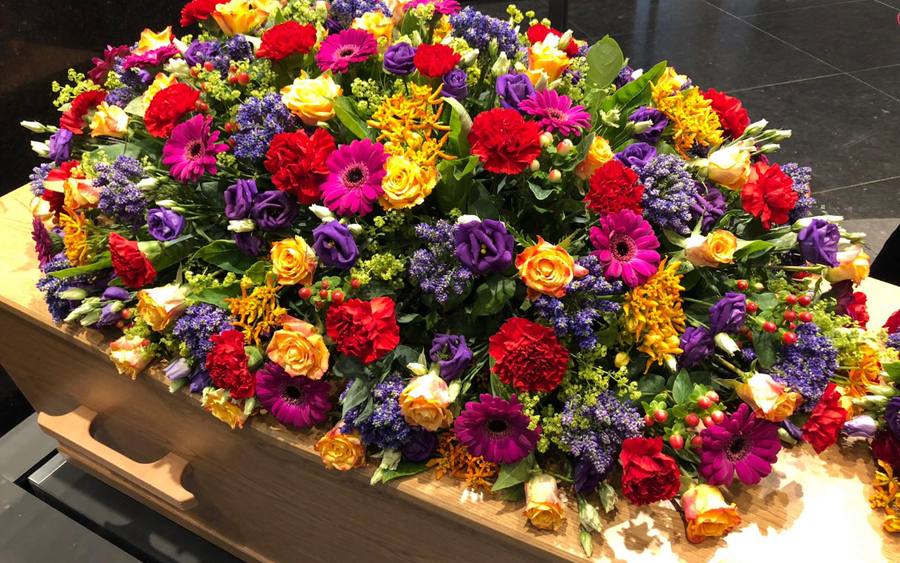 Een uitvaartkist met een groot bloemstuk in rood, geel en paars