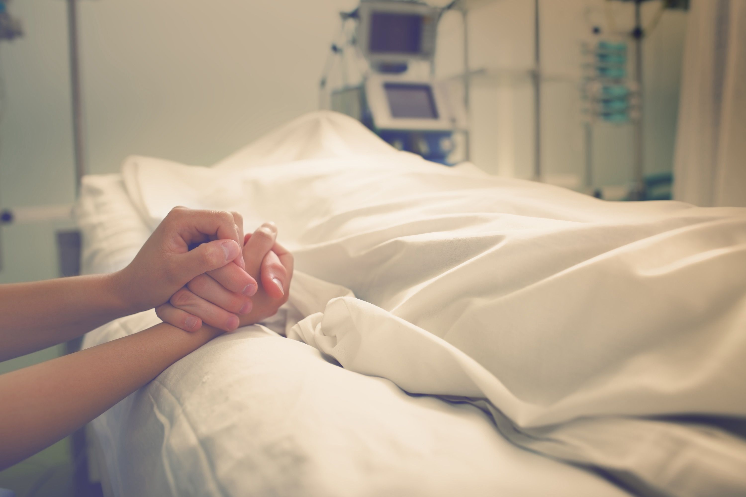 Twee handen die elkaar vasthouden op de rand van een ziekenhuisbed