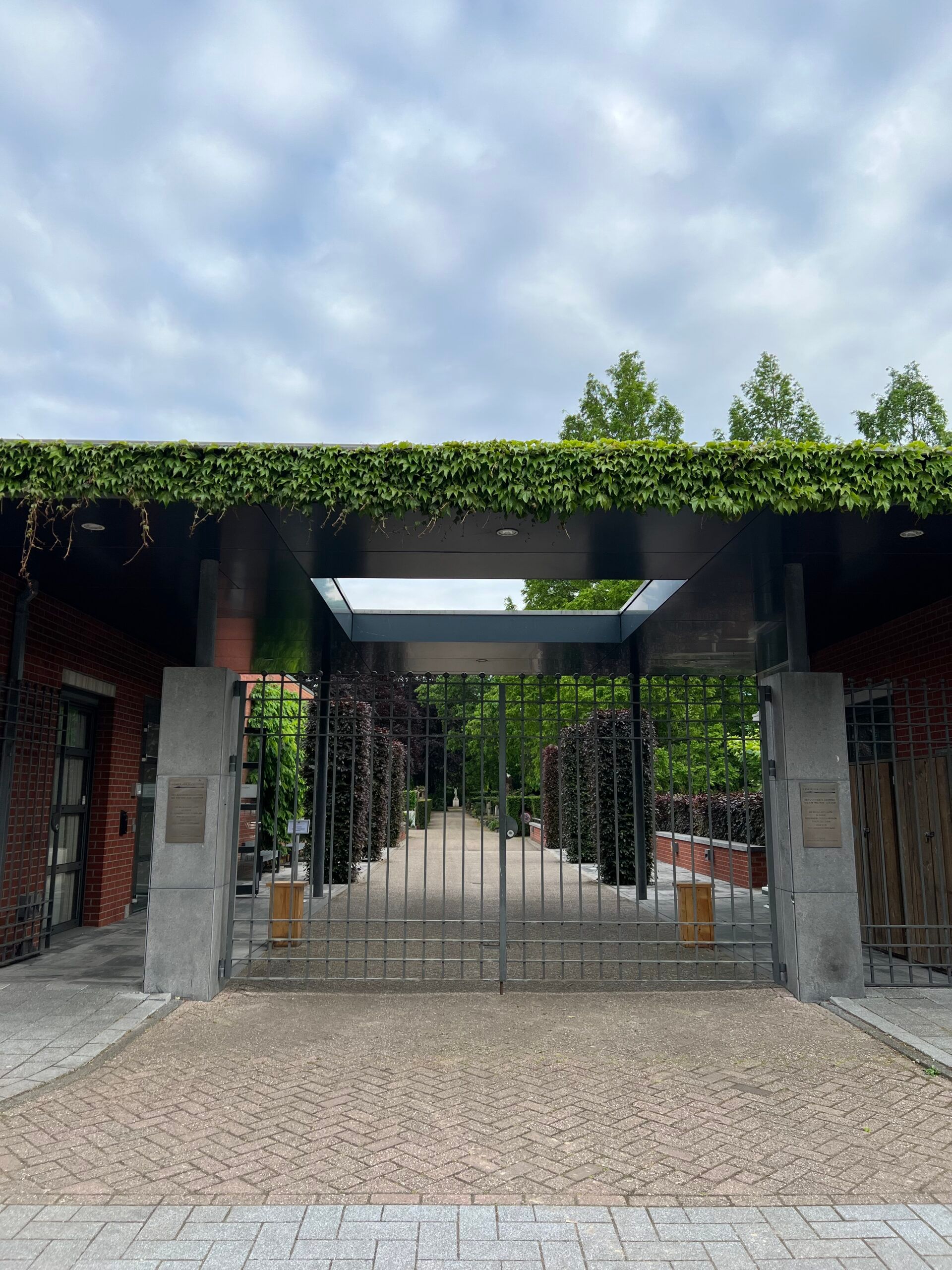 Een poort begroeid met klimop aan de ingang van begraafplaats Buitenveldert