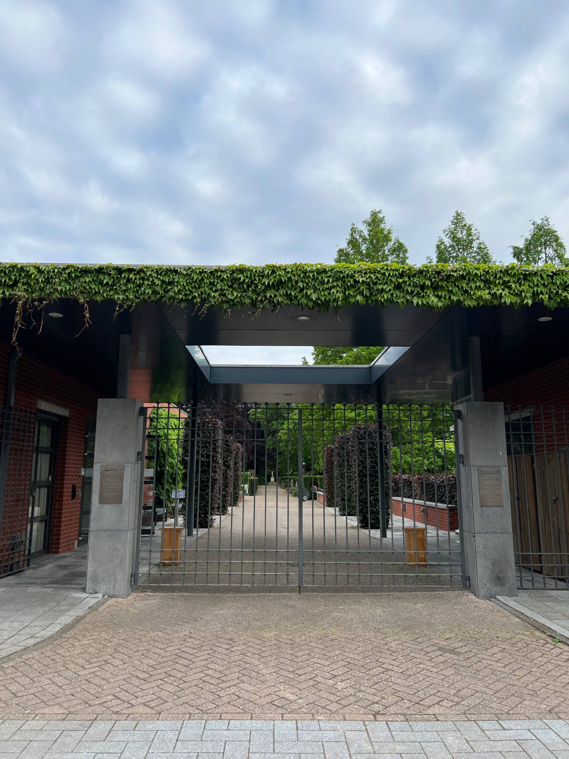 Een poort begroeid met klimop aan de ingang van begraafplaats Buitenveldert