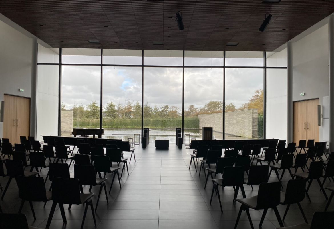 De ceremonieruimte van Crematorium Duin- en Bollenstreek, met stoelen in rijen voor een glazen wand