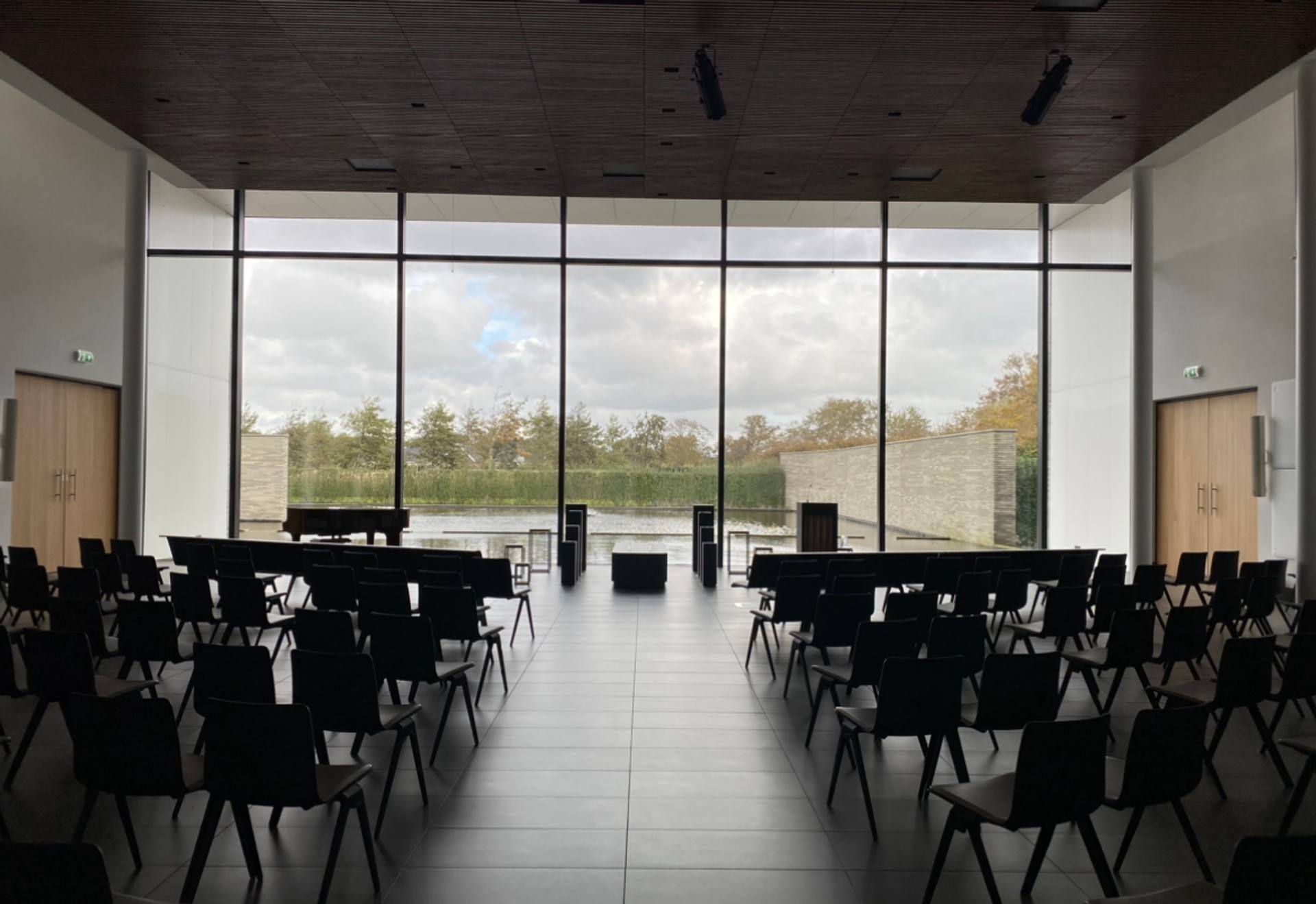 De ceremonieruimte van Crematorium Duin- en Bollenstreek, met stoelen in rijen voor een glazen wand