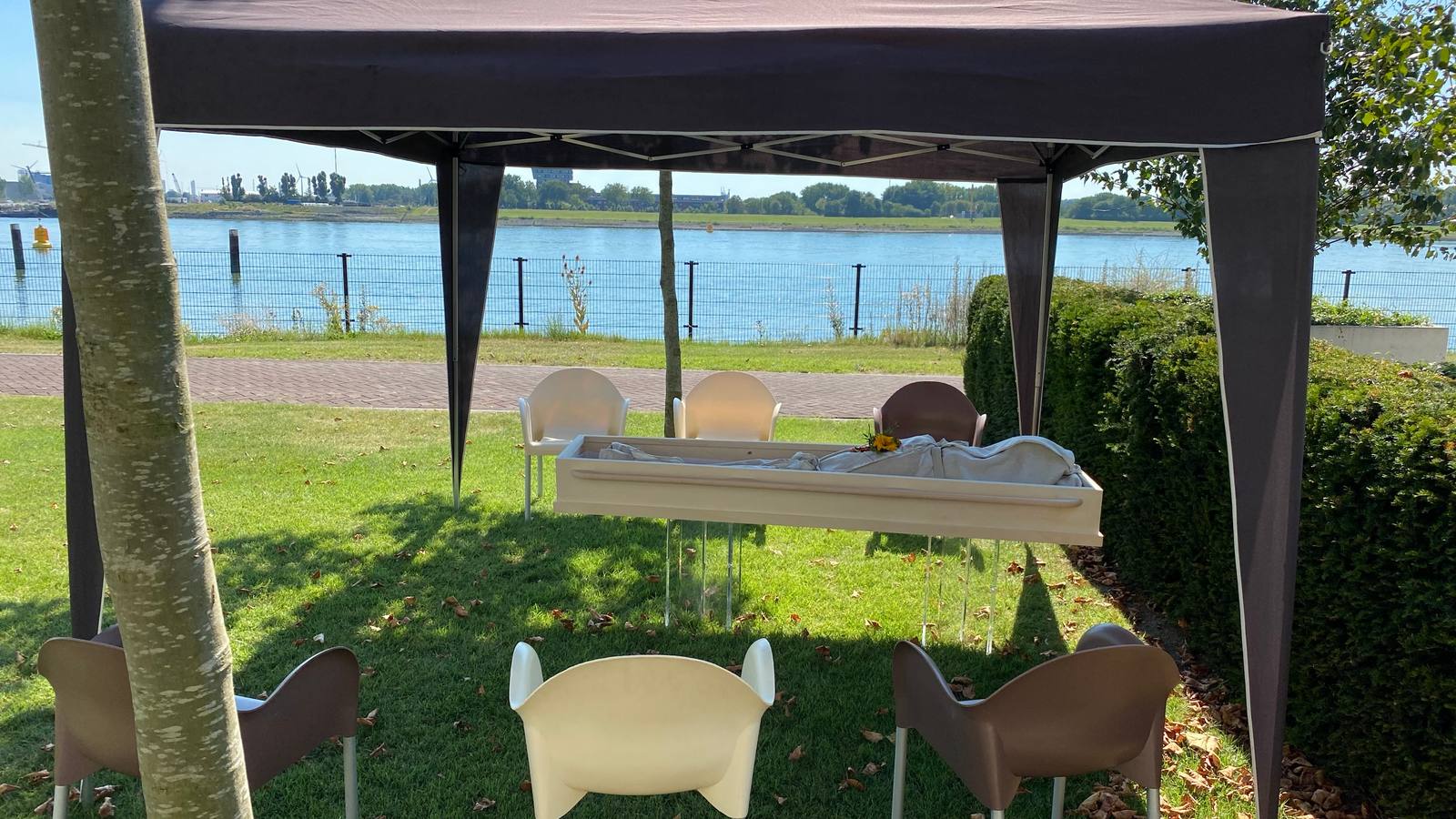 Een tent aan het water met stoelen in rijen en een opbaring vooraan
