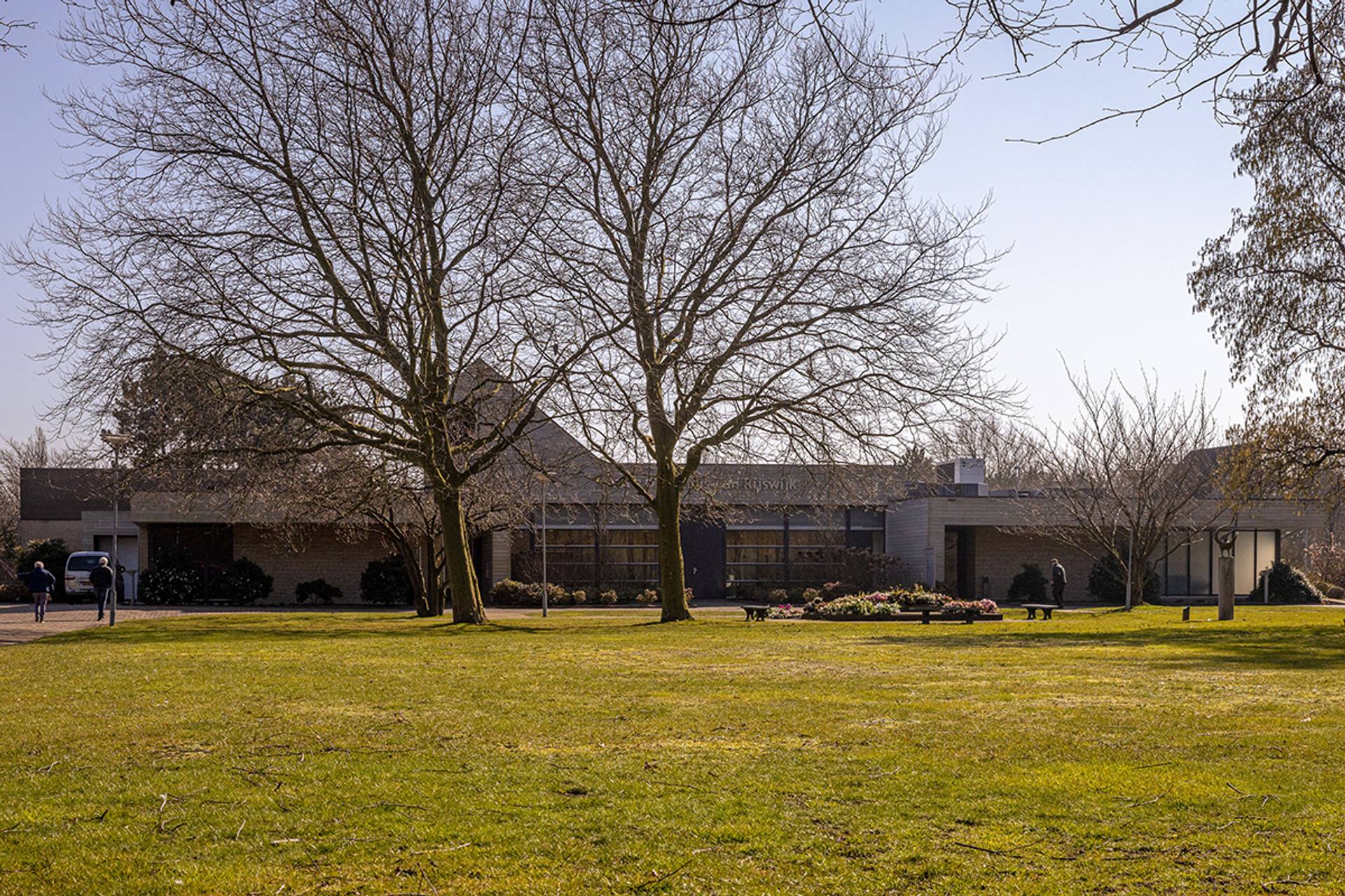 Het lage gebouw van Eikelenburg in Rijswijk, achter een grasveld met bomen