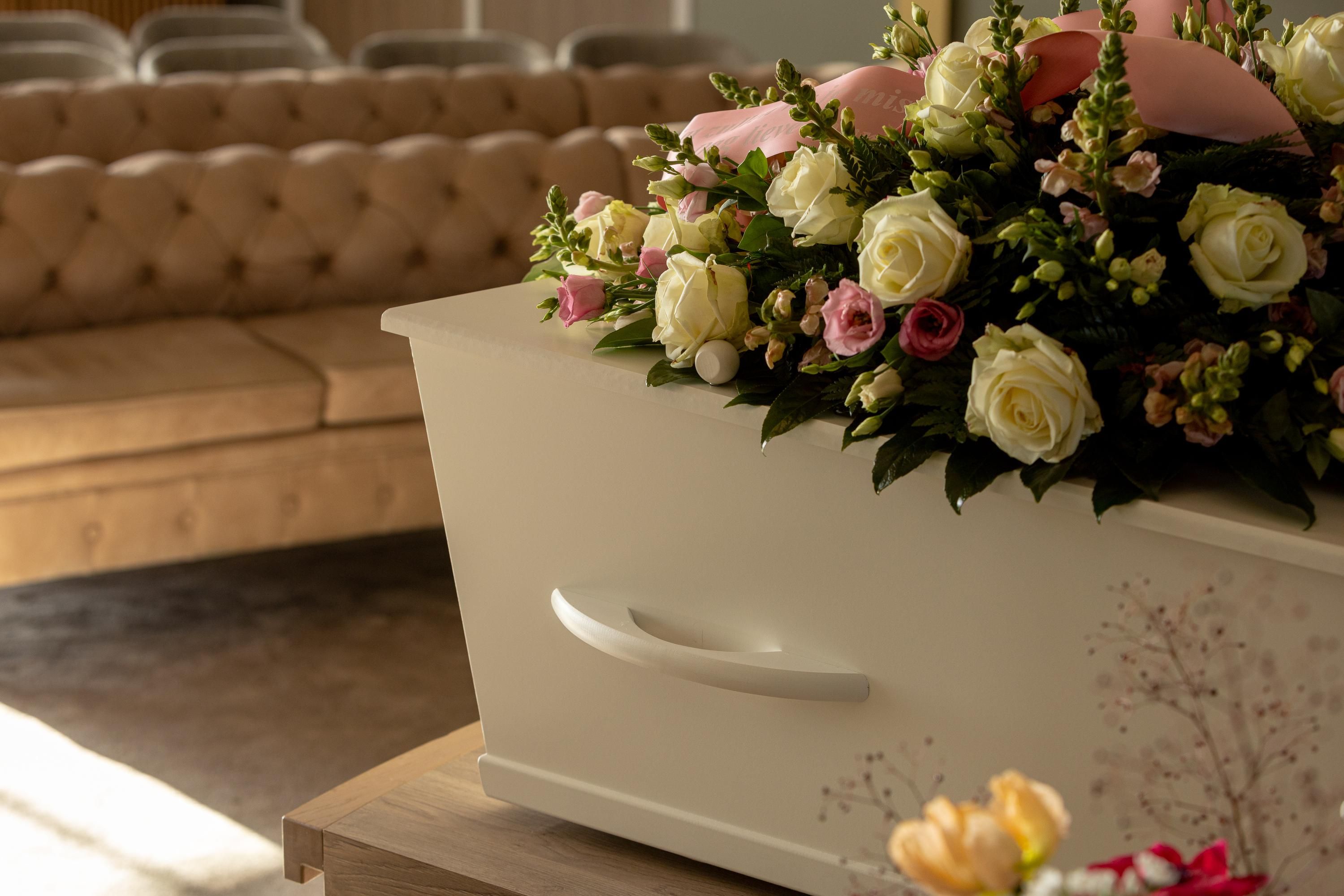 Een crèmekleurige uitvaartkist met witte en roze rozen in een warme kamer