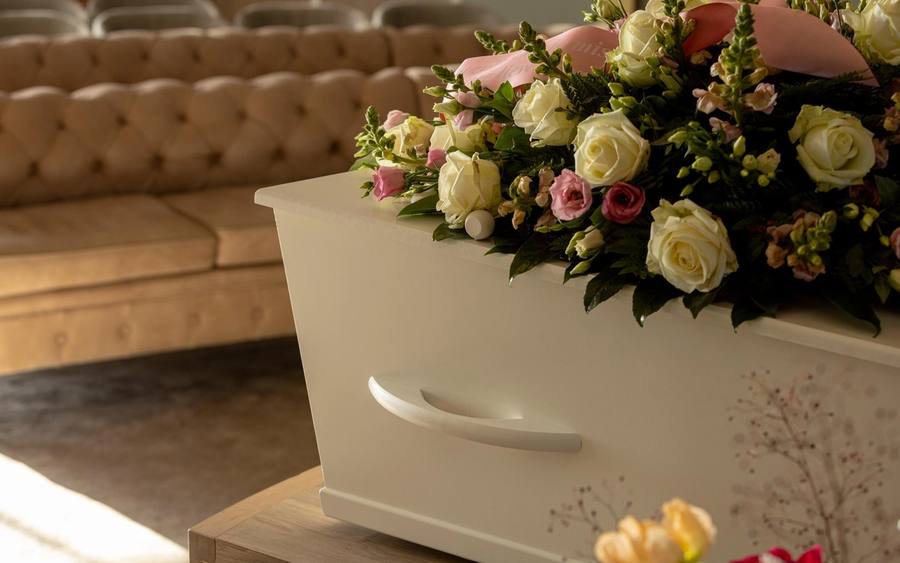 Een crèmekleurige uitvaartkist met witte en roze rozen in een warme kamer