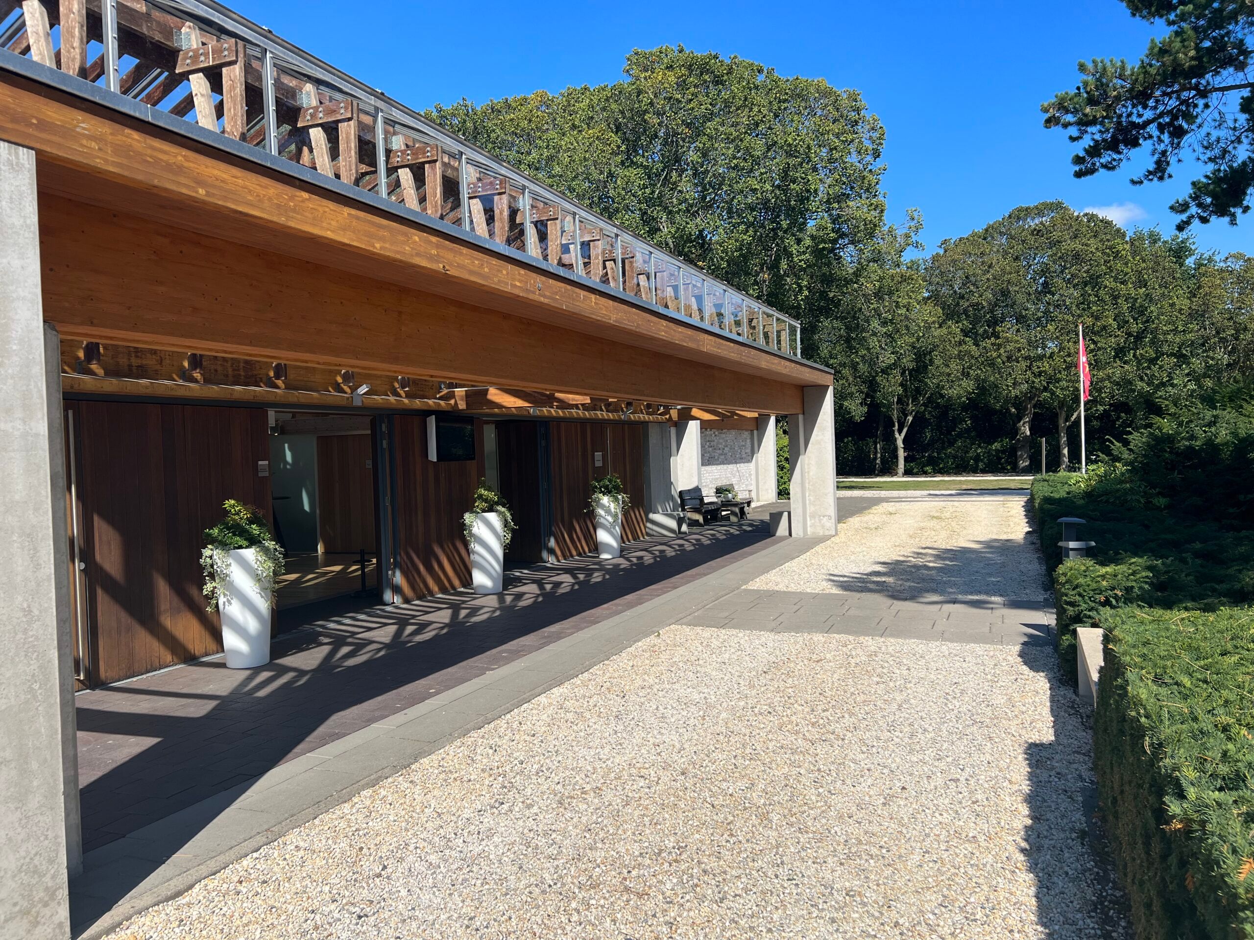 De lange houten overkapping langs de entree van Crematorium DELA Kennemerland, met een grindpad ervoor