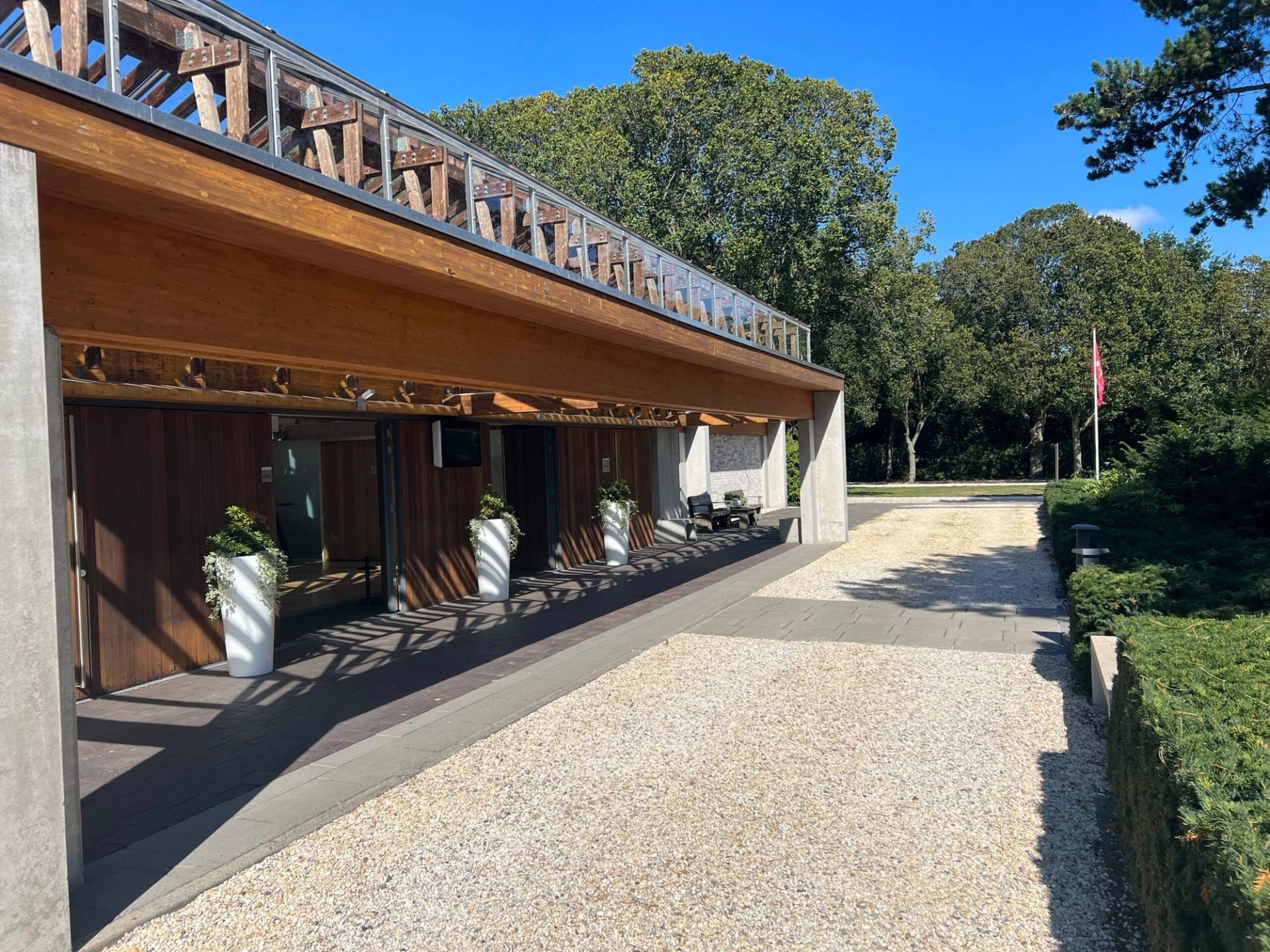 De lange houten overkapping langs de entree van Crematorium DELA Kennemerland, met een grindpad ervoor