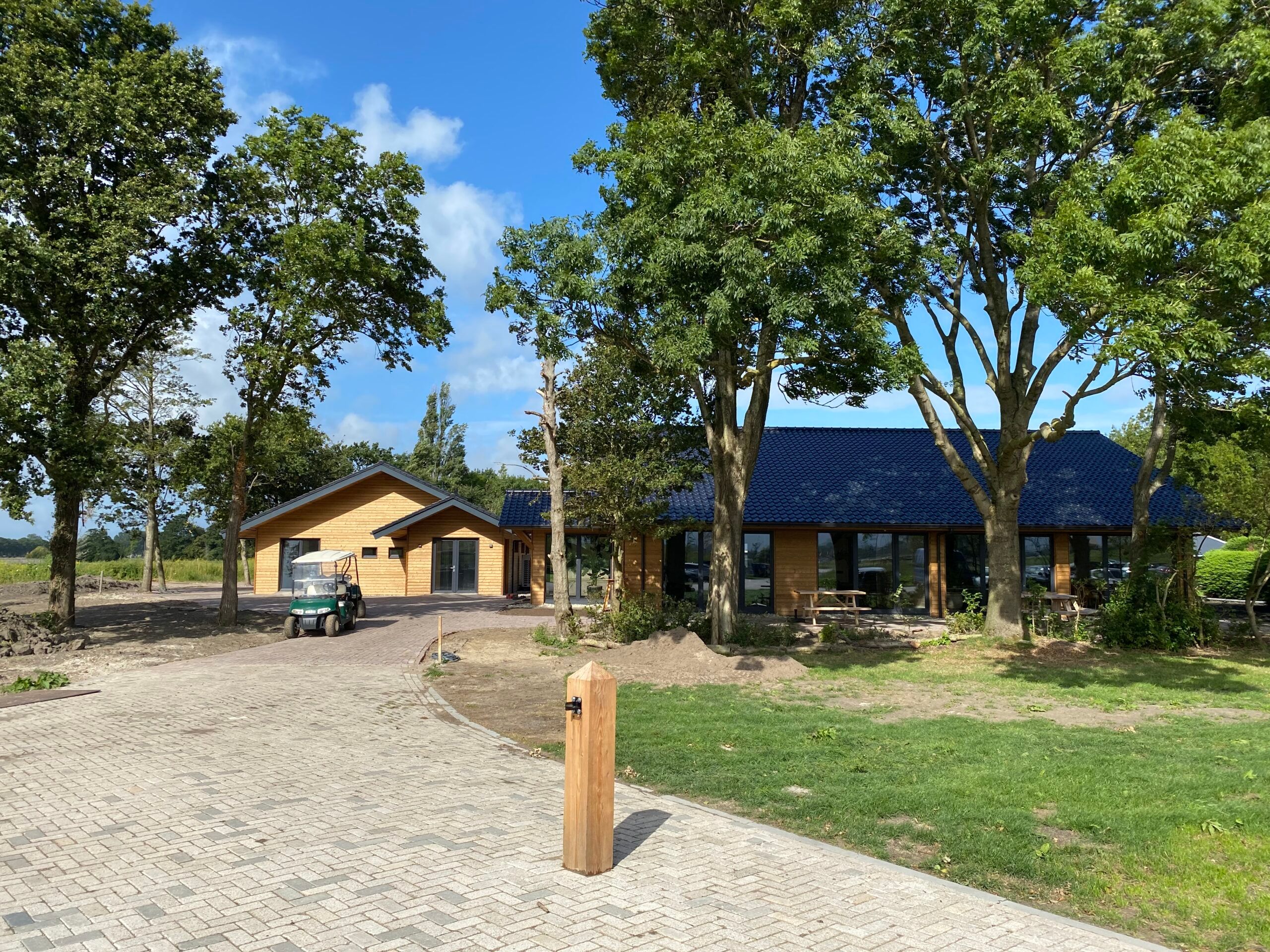 Het houten gebouw van Natuurbegraafplaats Geestmerloo, met een blauw dak tussen de bomen