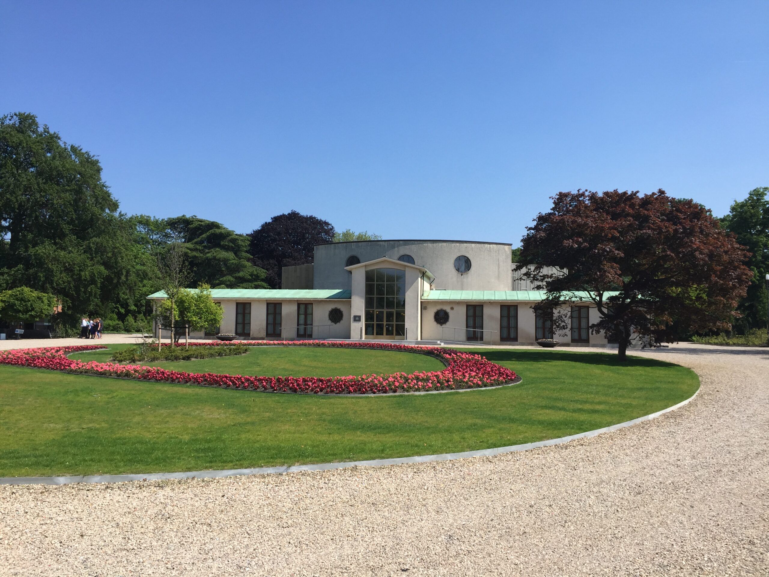 Het gebouw van De Nieuwe Ooster achter een rond bloemperk met rode bloemen