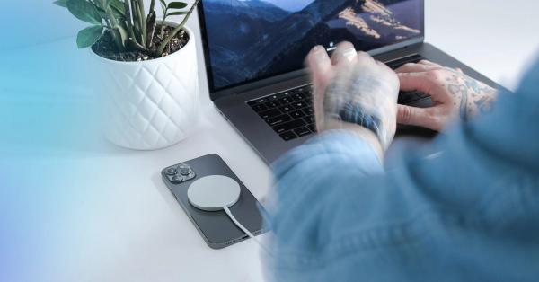 観葉植物とスマートフォンが置かれたデスクでノートパソコンを操作する手