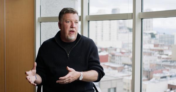 A Guardant Health security leader speaking in a video interview, city skyline behind