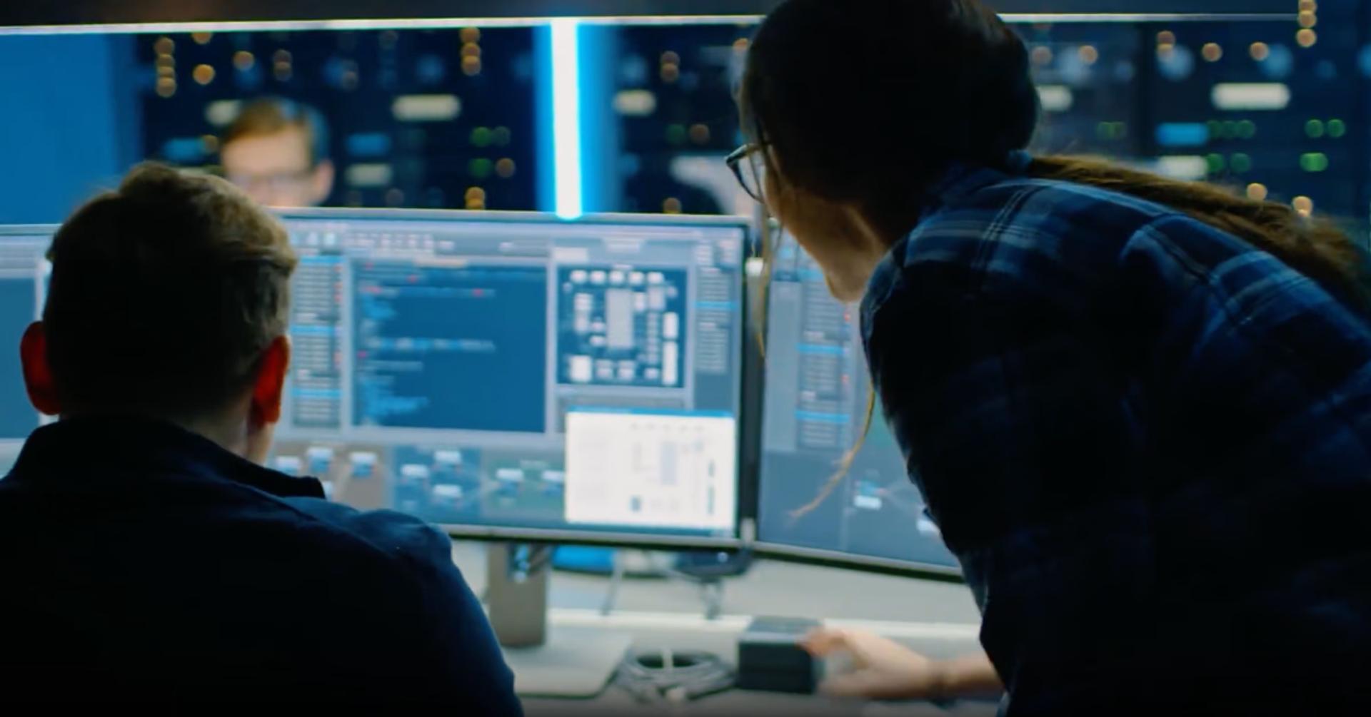 Two analysts at a monitor in a darkened security operations centre