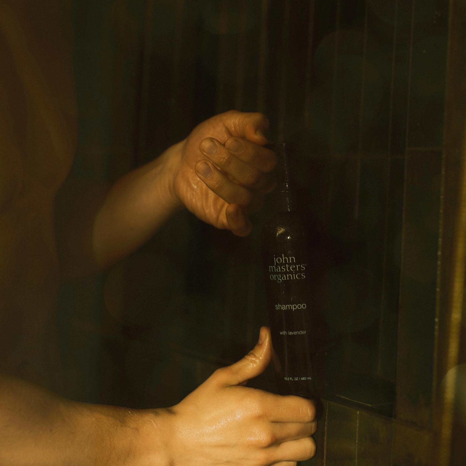 Guy in shower holding a John Masters Organics Shampoo bottle