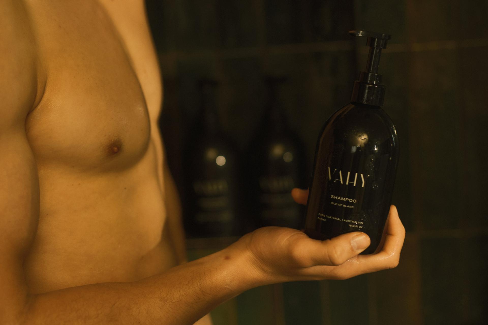 Man in shower holding Vahy Isle of Blanc Shampoo dispenser in hand
