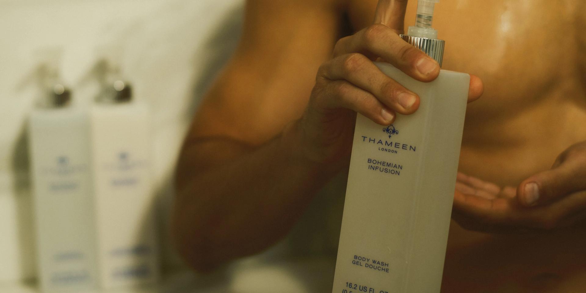 Man in shower holding Thameen London Body Wash dispenser in hand