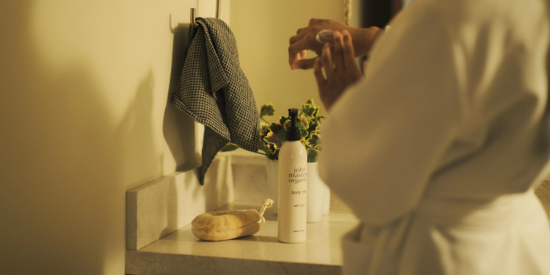 John Masters Organics Body Milk on bathroom vanity, girl trying some on hand