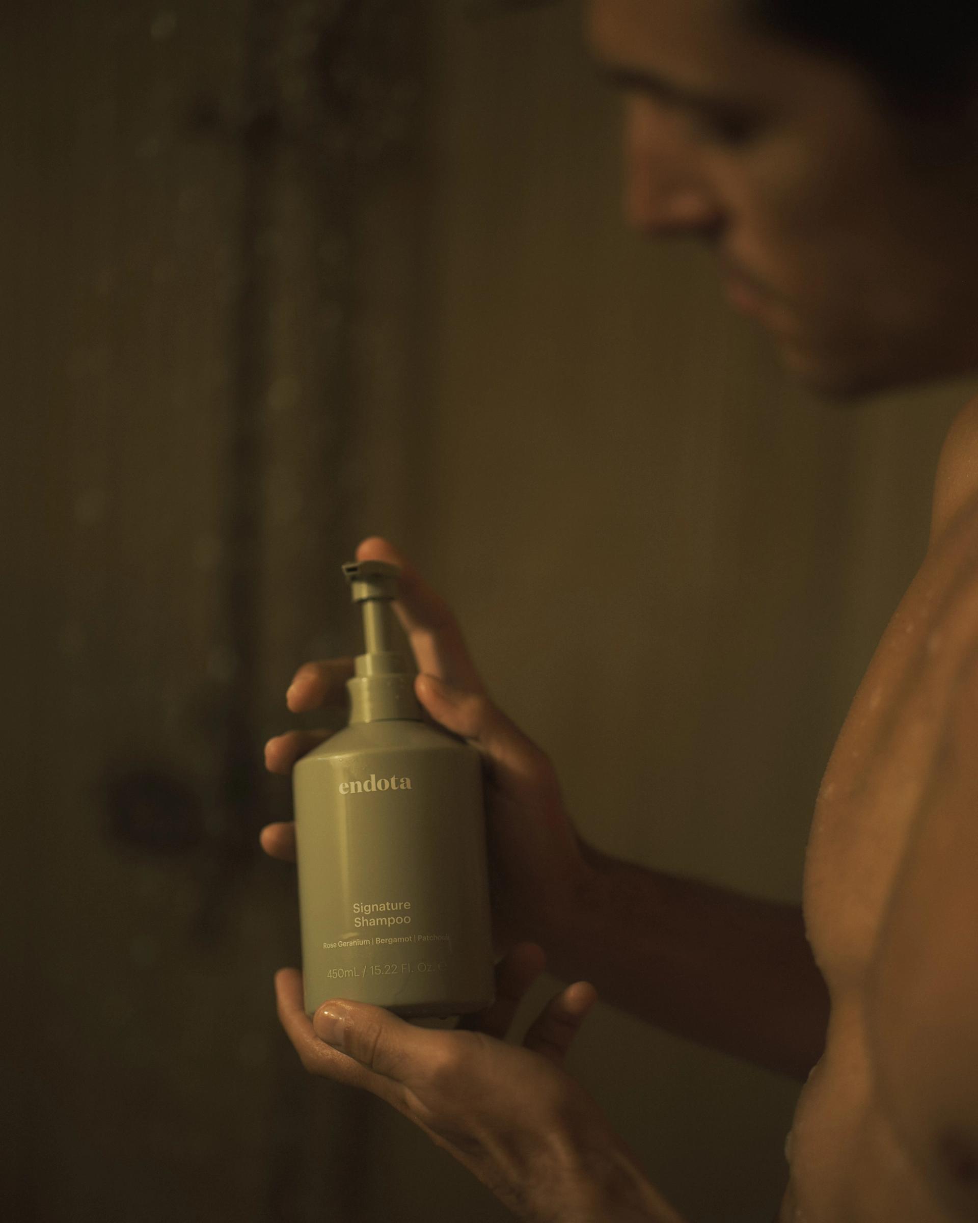 Guy in Shower holding a bottle of endota Signature Shampoo