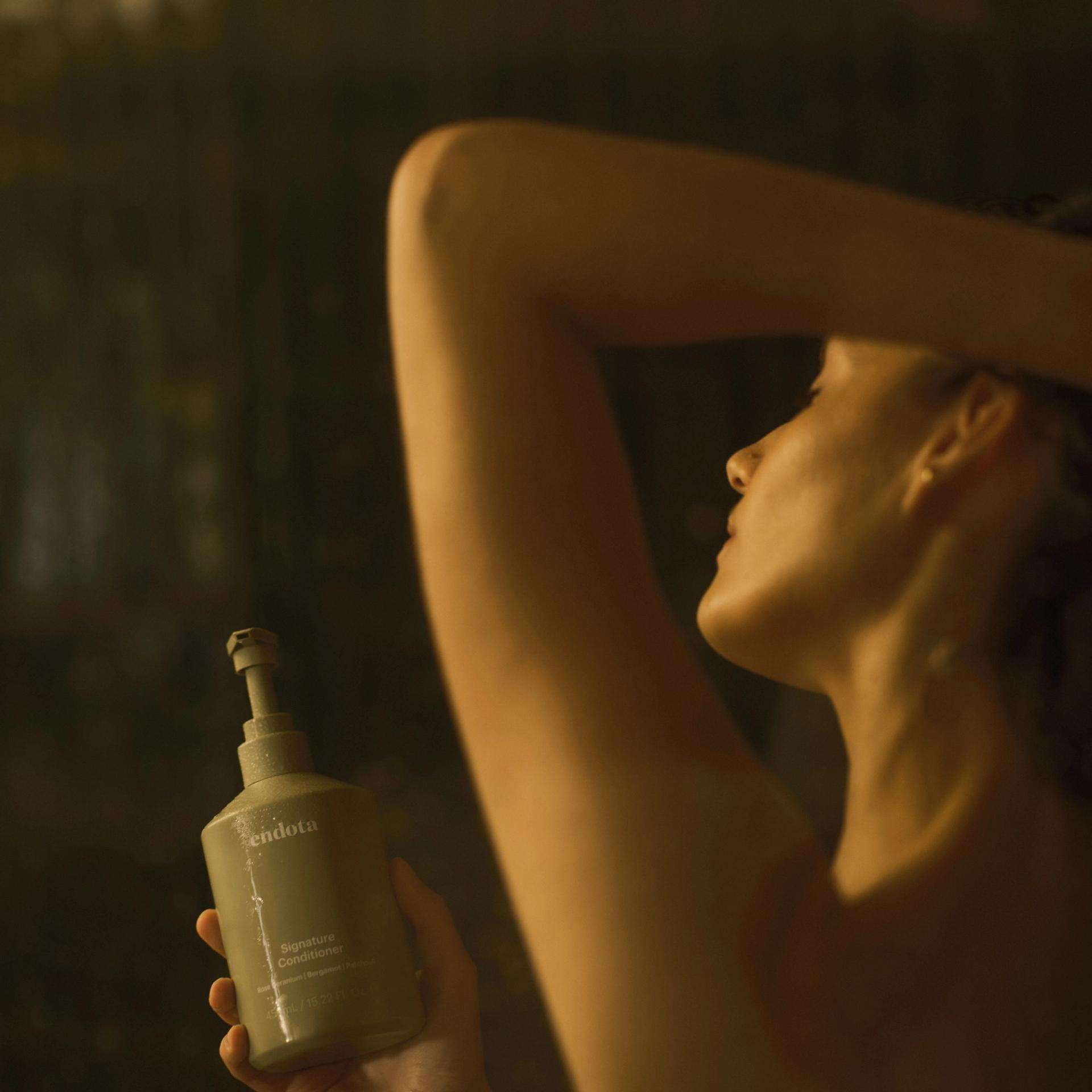 Girl in Shower holding a bottle of endota Signature Conditioner