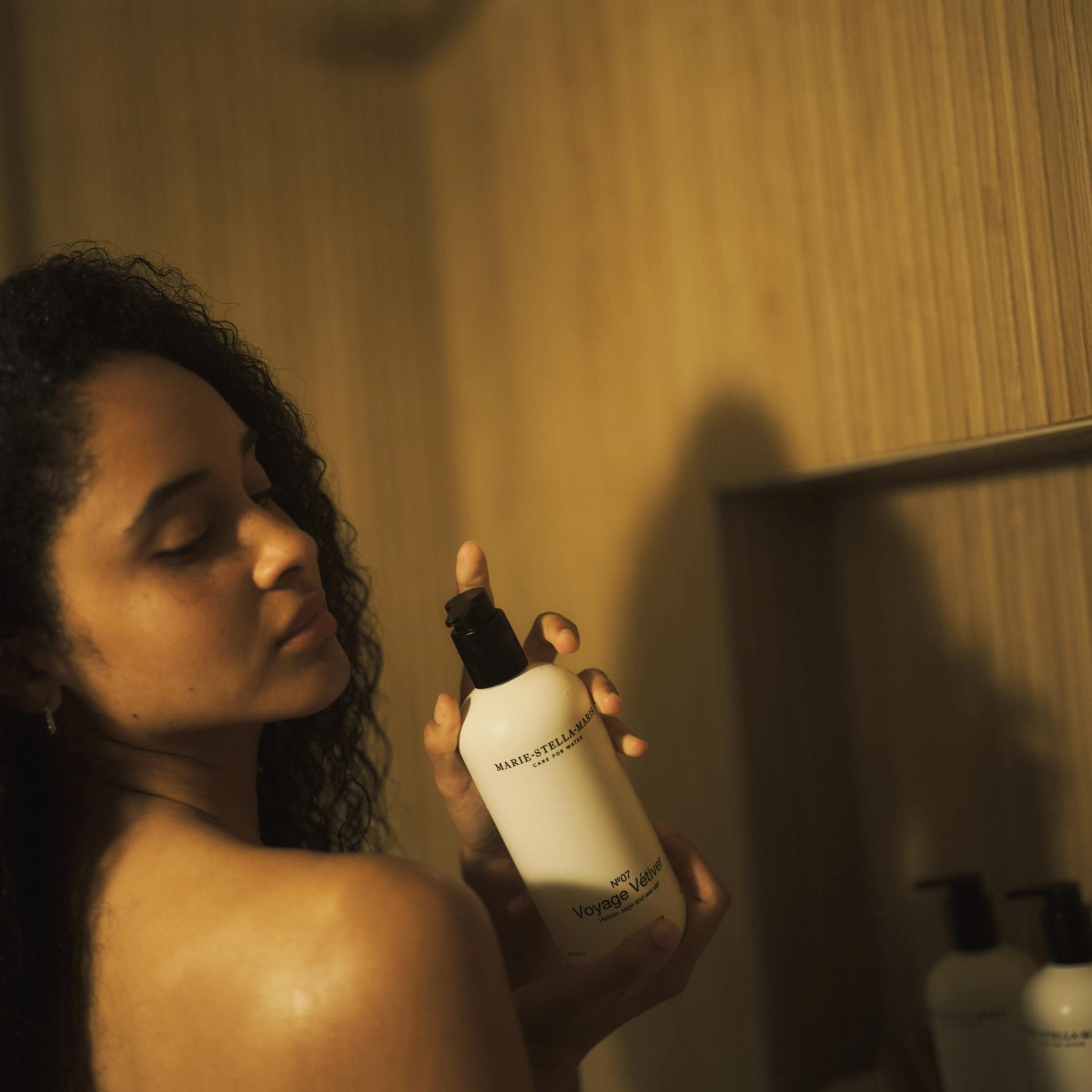 Woman in shower holding Marie Stella Maris Voyage Vetiver Body Wash dispenser in hands