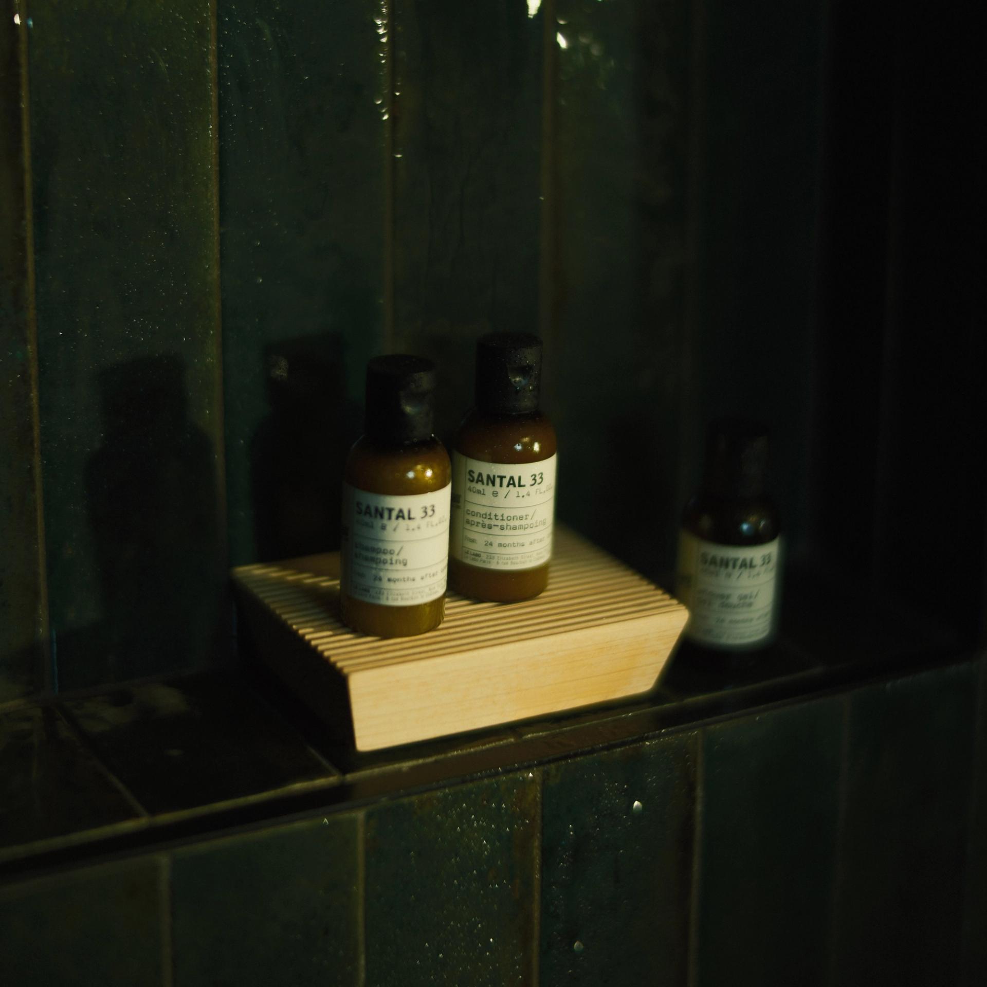 Le Labo Santal 33 Shampoo, Conditioner and Shower Gel single-use amenities on shower shelf