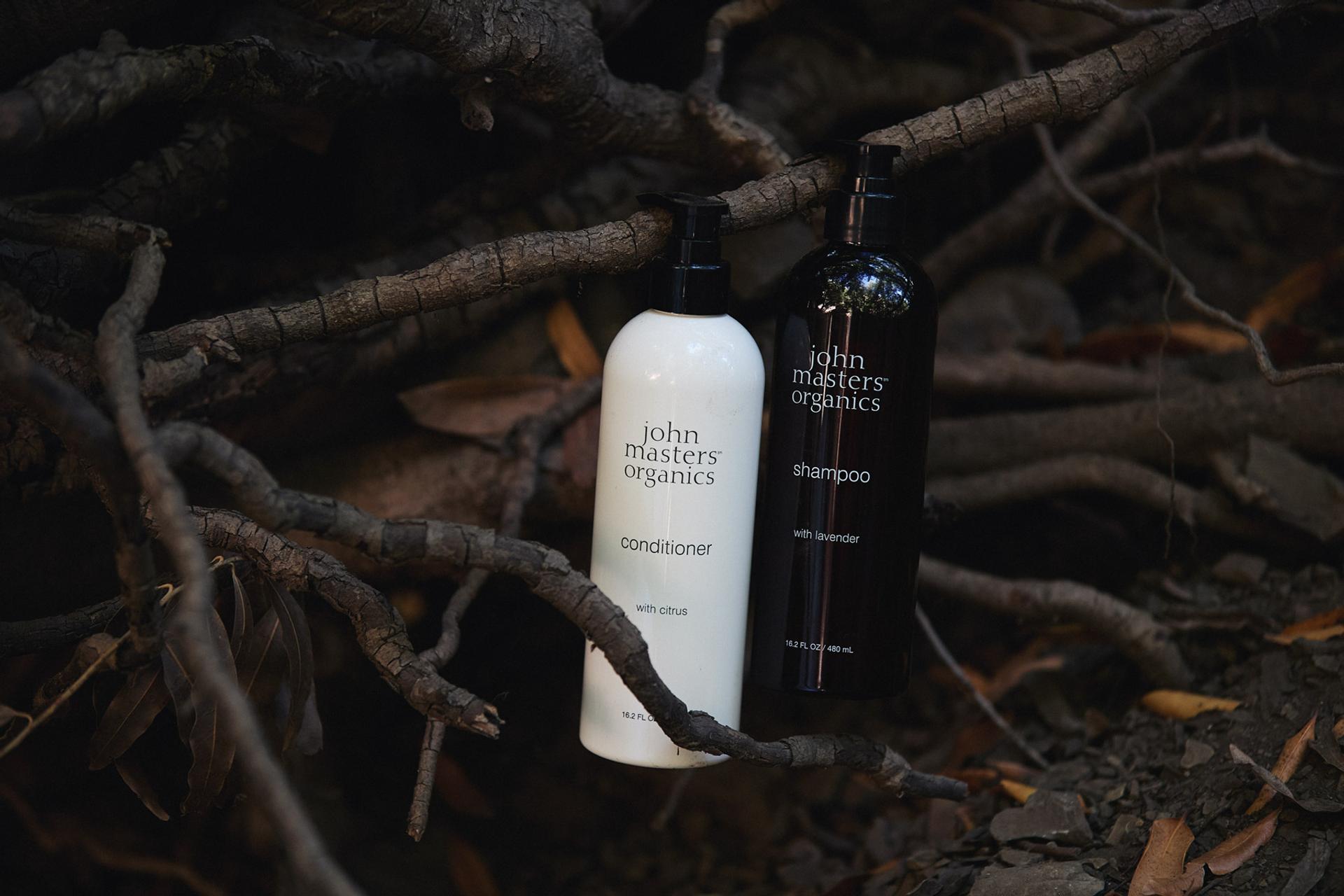 John Masters Organics Shampoo and Conditioner bottles sitting on tree bark outdoors