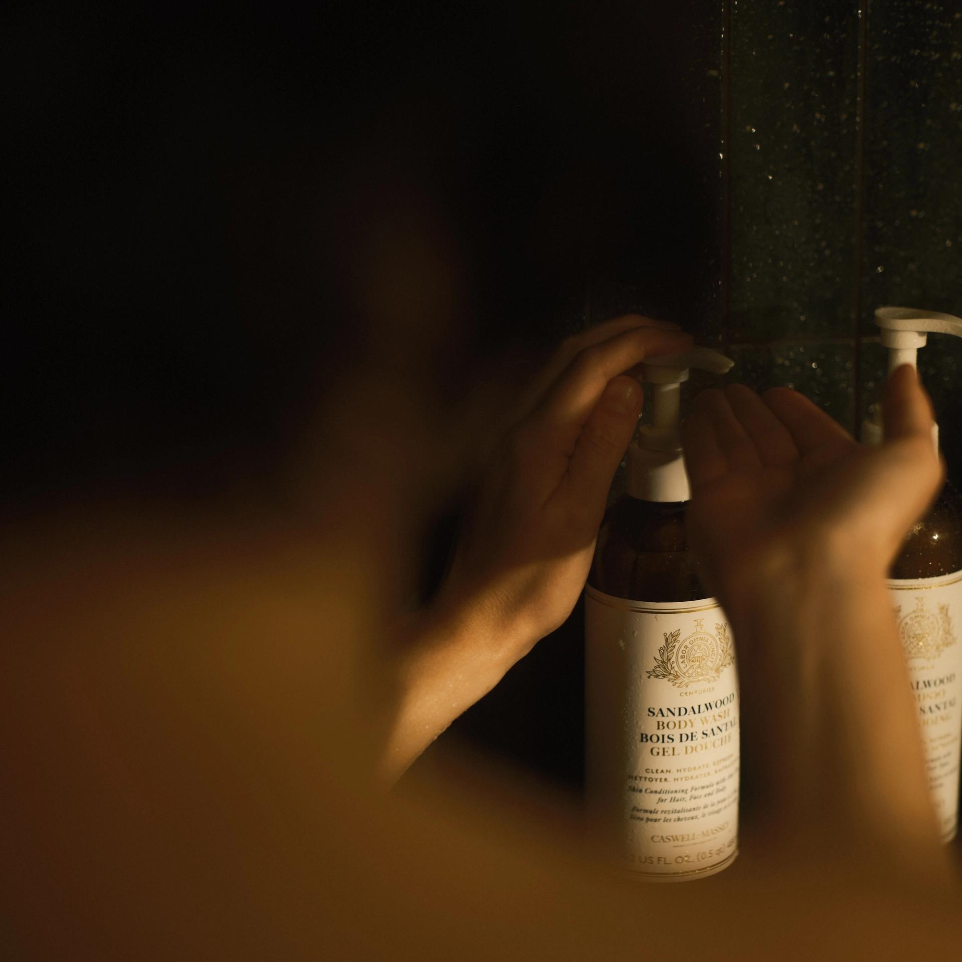 Guy pumping bottle of Caswell-Massey Sandalwood Body Wash in the shower