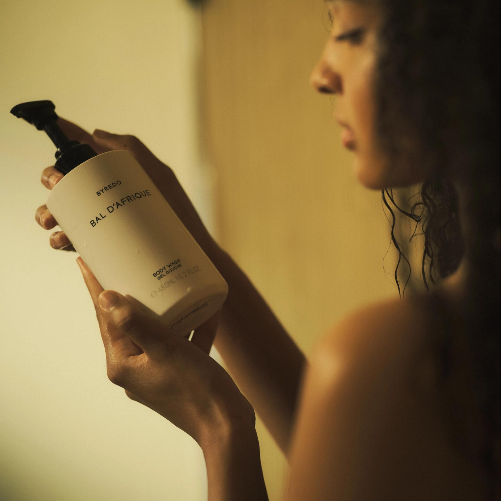 Girl holding a bottle of Byredo Bal d'Afrique Body Wash in the shower