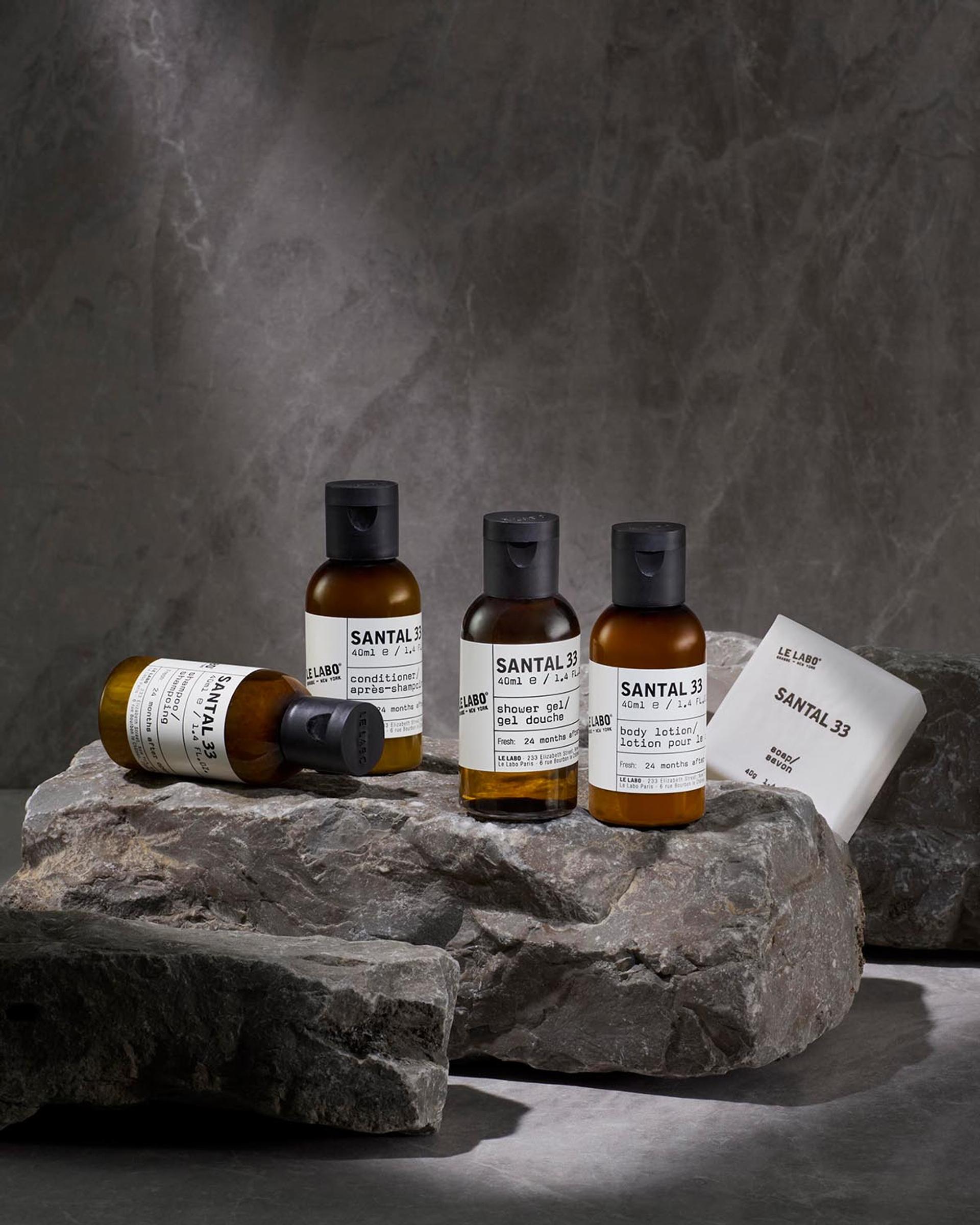 Le Labo Santal 33 Shampoo, Conditioner, Shower Gel, Body Lotion and Bar Soap single-amenities on counter with rock