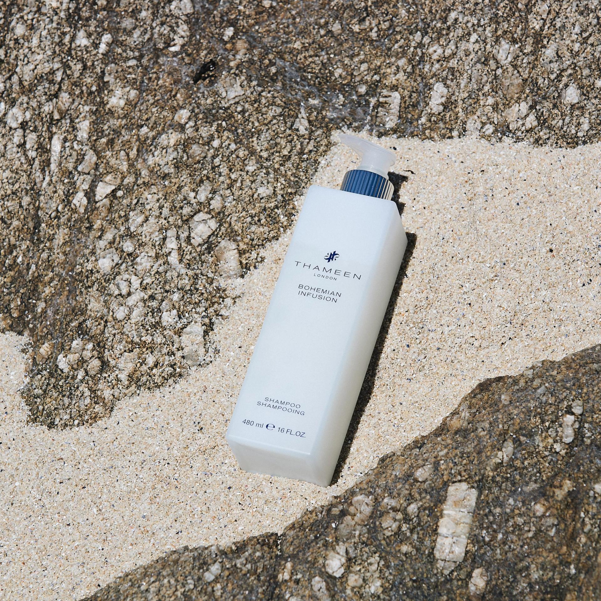 Thameen London Bohemian Infusion Shampoo dispenser laying flat on sand and rock on beach
